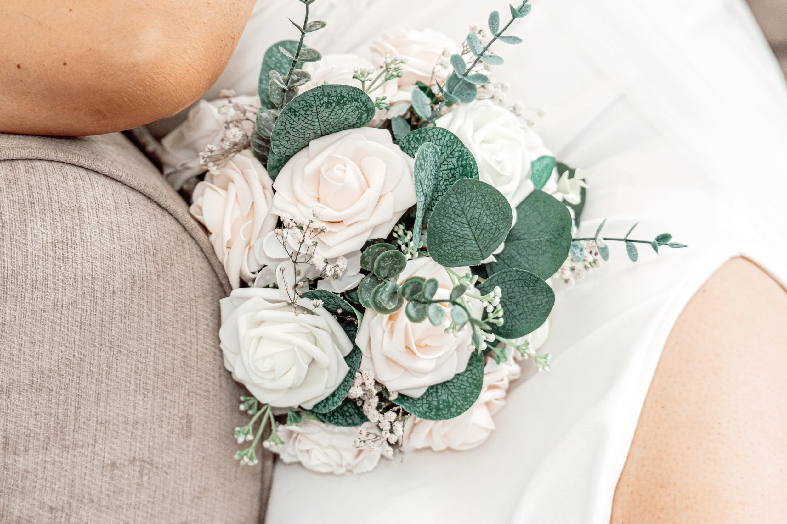 Close-up of a bouquet of white roses and green foliage resting against a person's shoulder and hip, likely part of a wedding or formal occasion.
