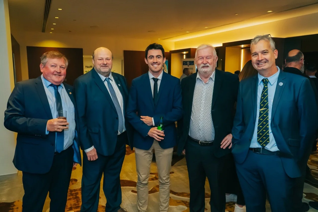 Five men in suits smiling at a formal event, standing in a hotel or conference center with warm lighting.