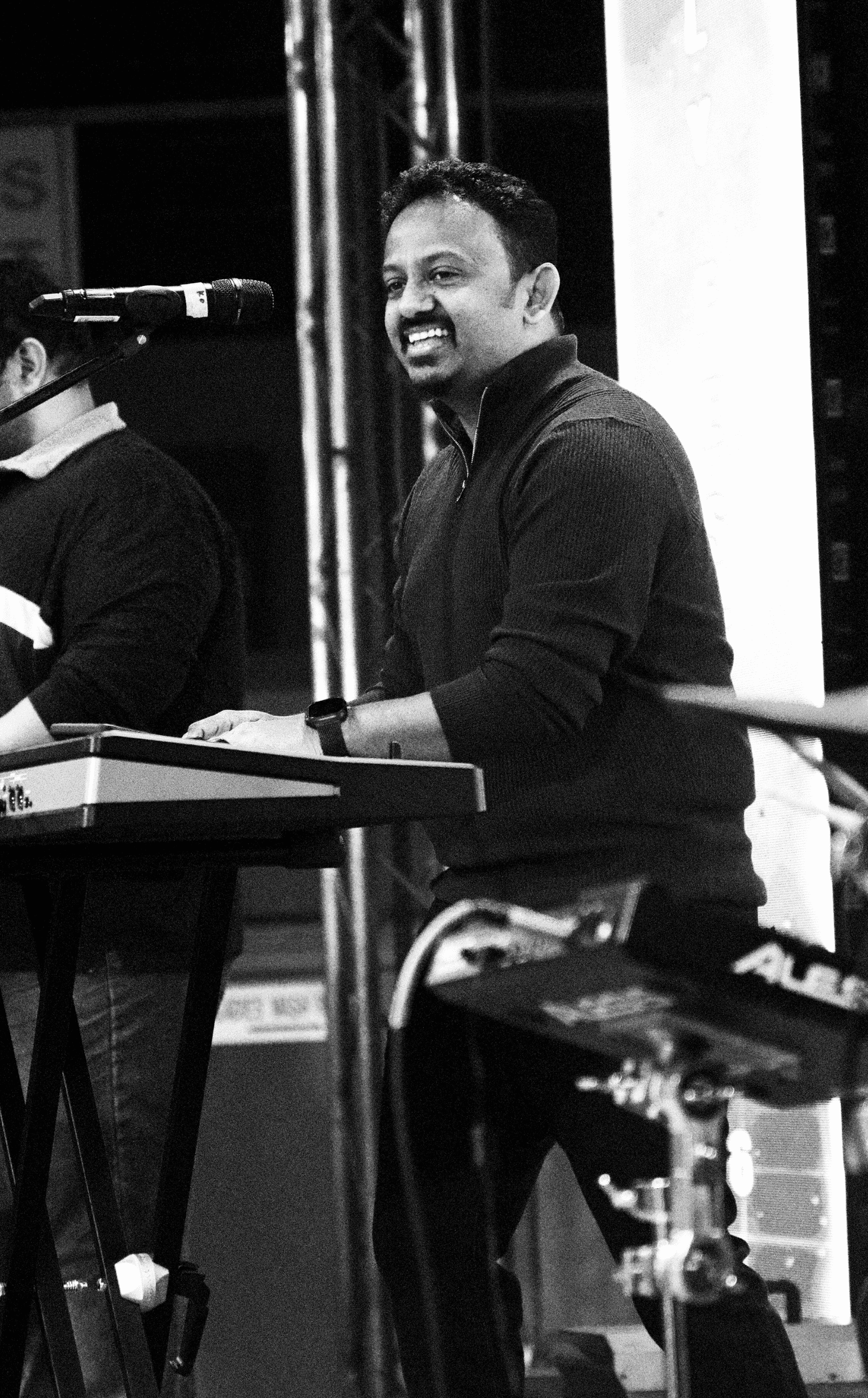 A man smiling while playing keyboard at an indoor event.