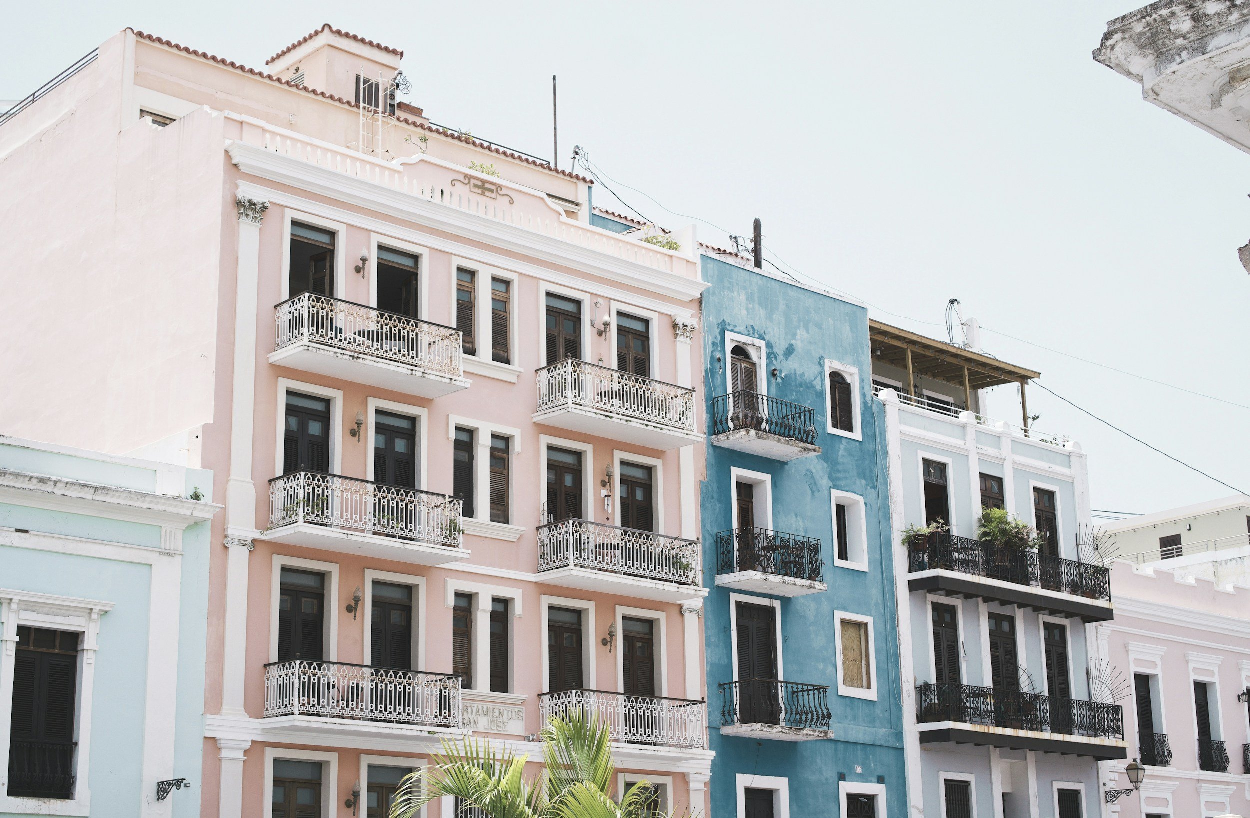 Colorful buildings with balconies in a city, featuring pink, blue, and white facades.