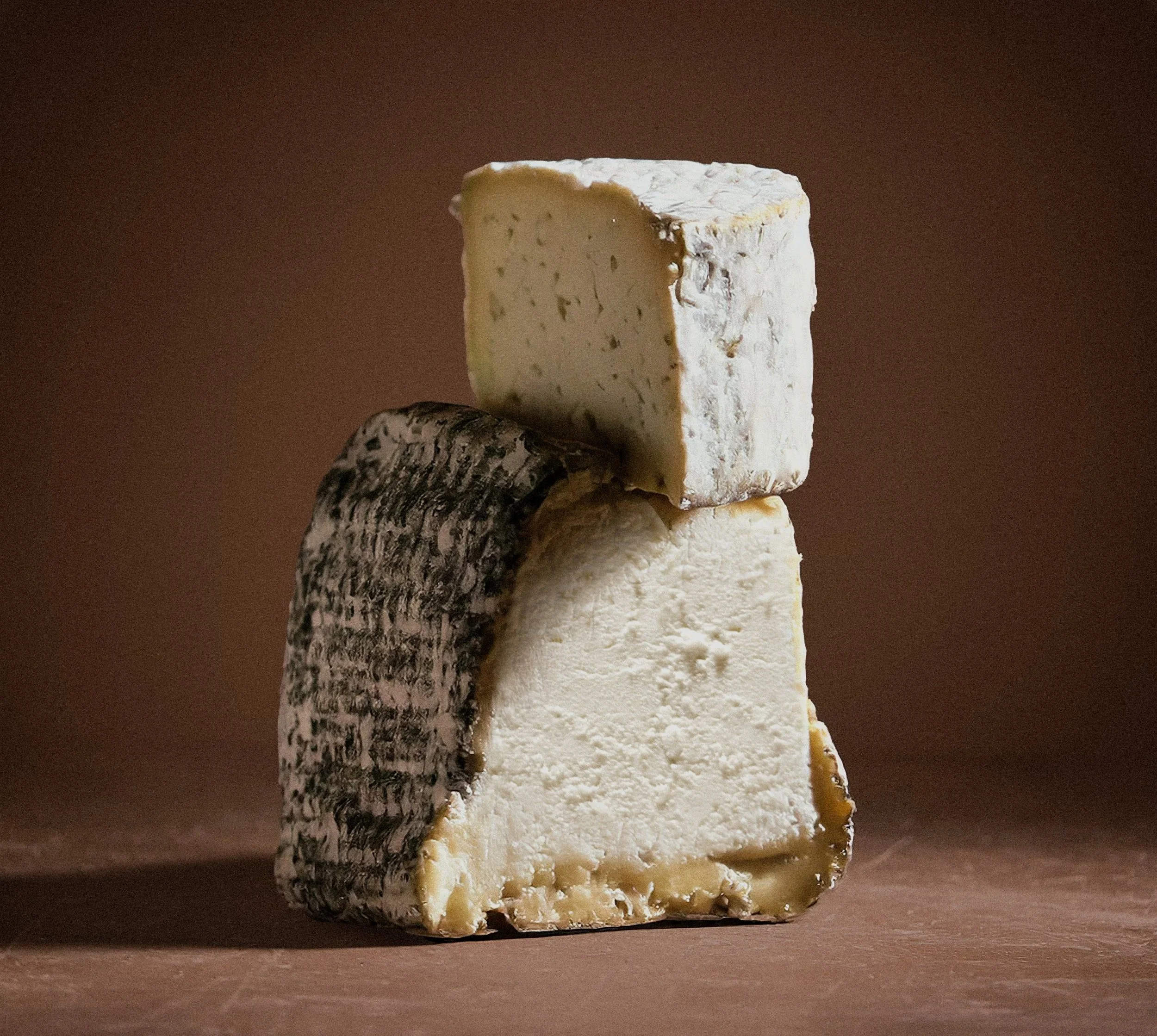 A stack of three different types of cheese on a wooden surface, with a brown background.