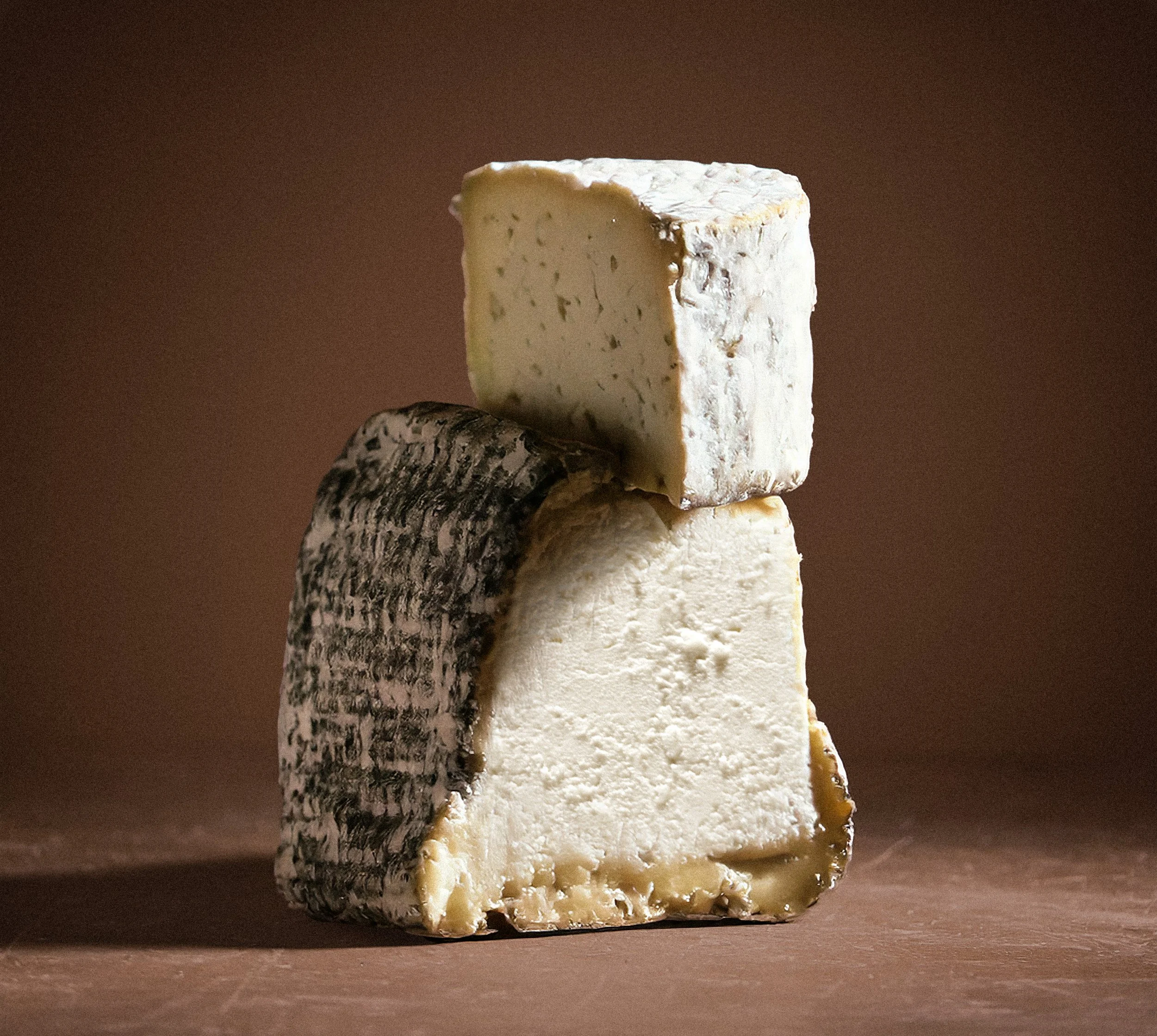 Three pieces of different cheeses stacked, with a brown background.