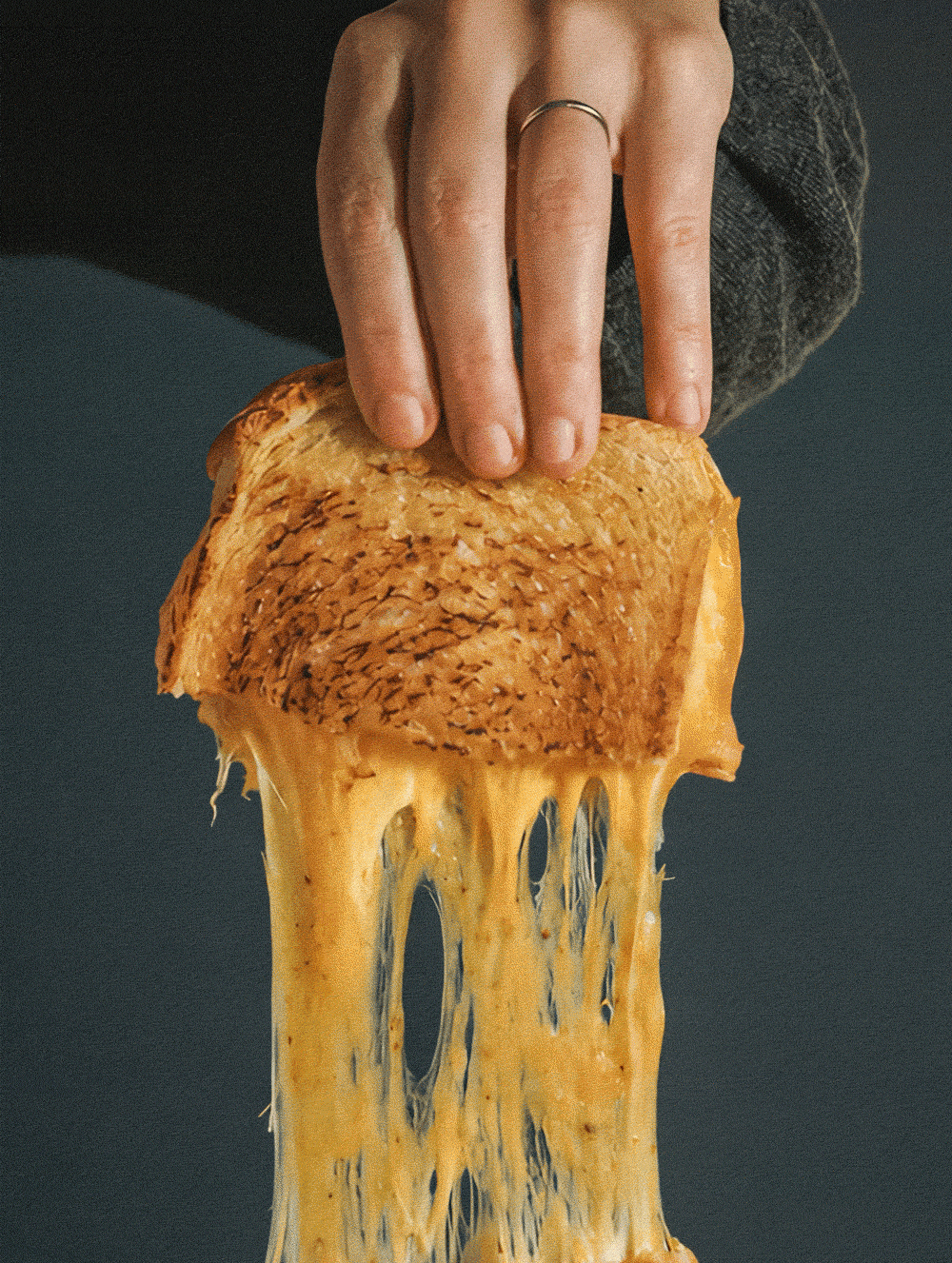 Person holding a hot, melted cheese toastie with gooey cheese stretching as it is pulled away.