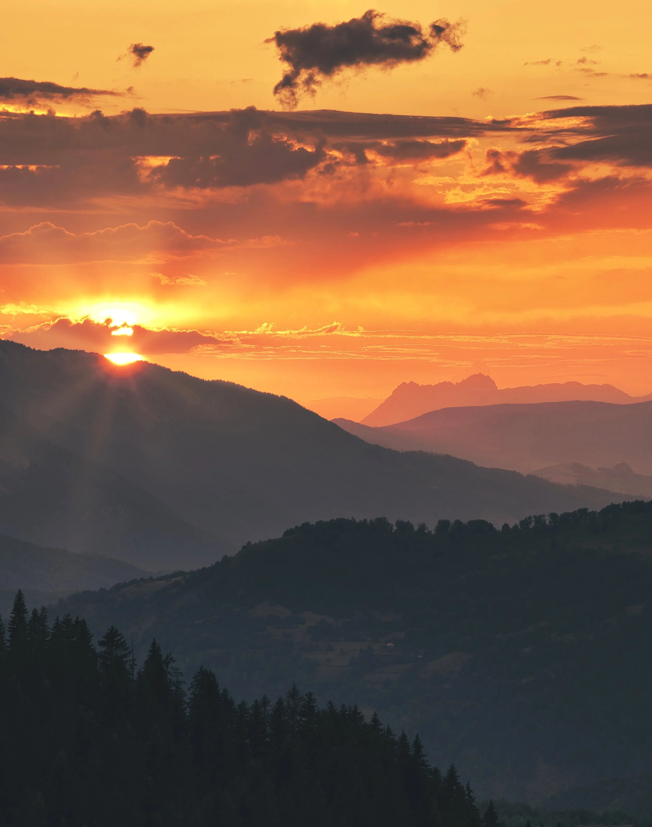 Sunset over layered Montenegrin mountains with orange and yellow sky and scattered clouds.