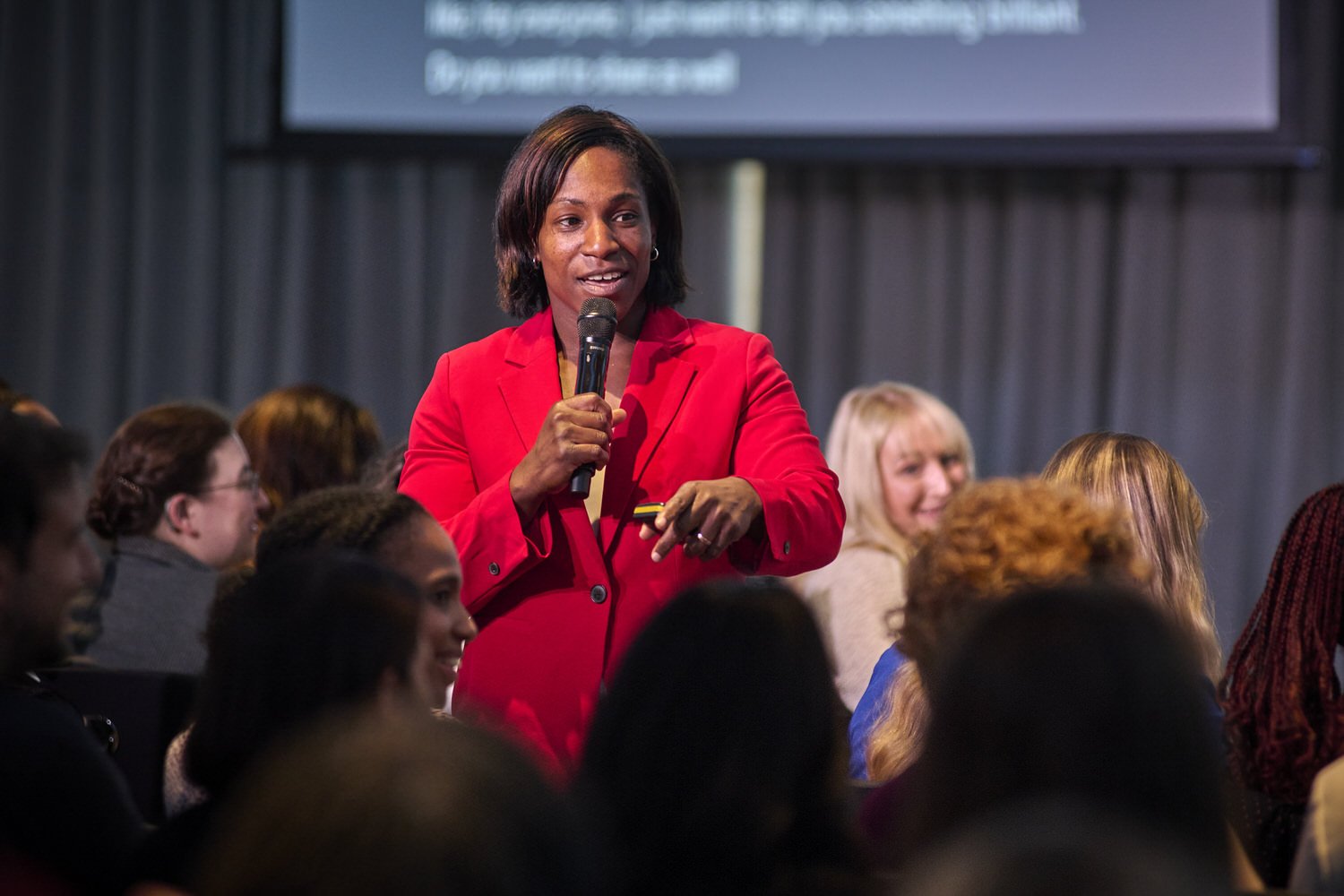 Lady in red jacket holding a microphone while speaking in the crowd.