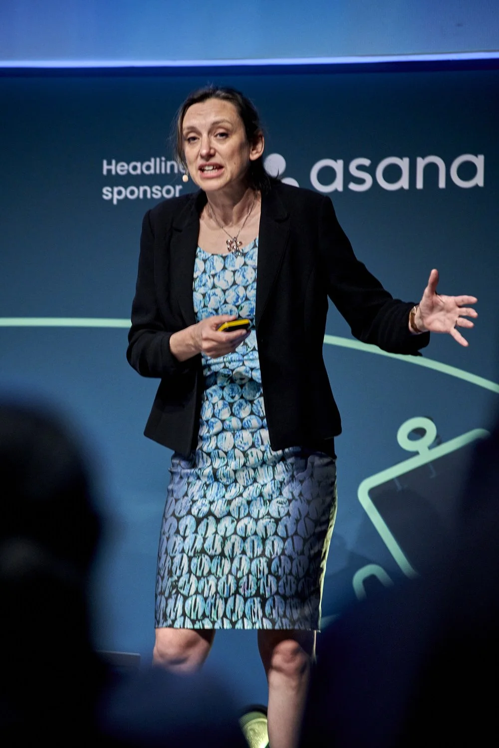 Lady gesturing on stage during conference presentation.