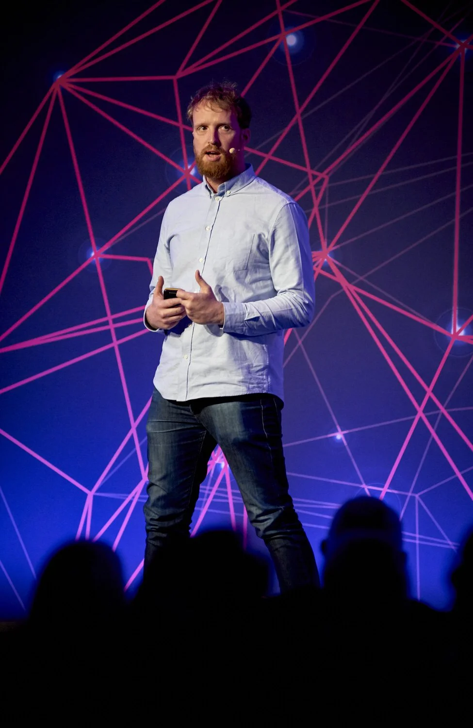 Man presenting on stage with red digital web graphic behind him.
