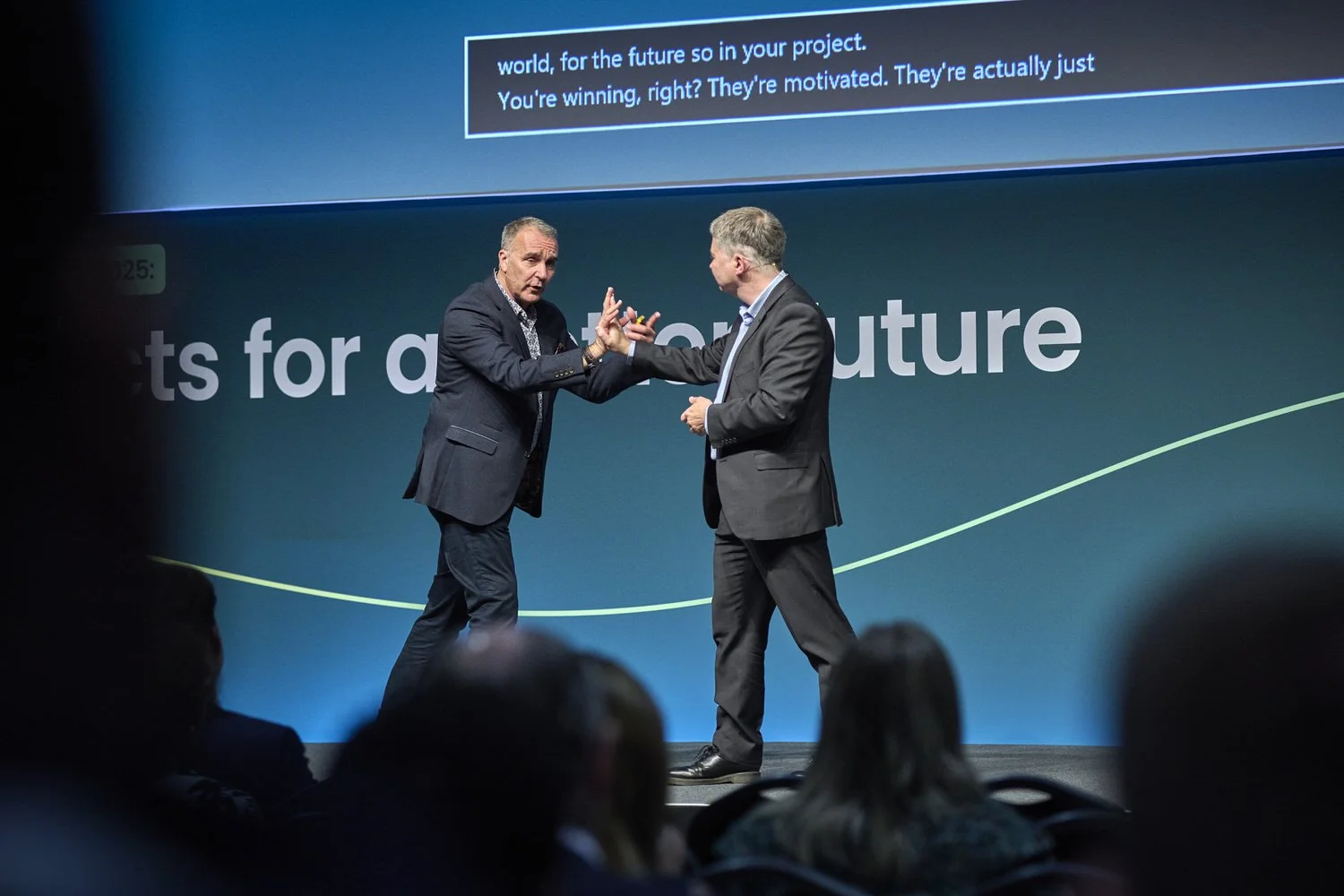 Two men on stage pressing hands together in demonstration.