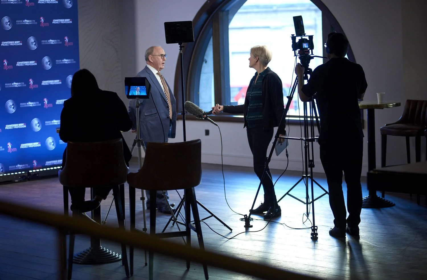 Video crew interviewing a man in front of a bright window at a business event.