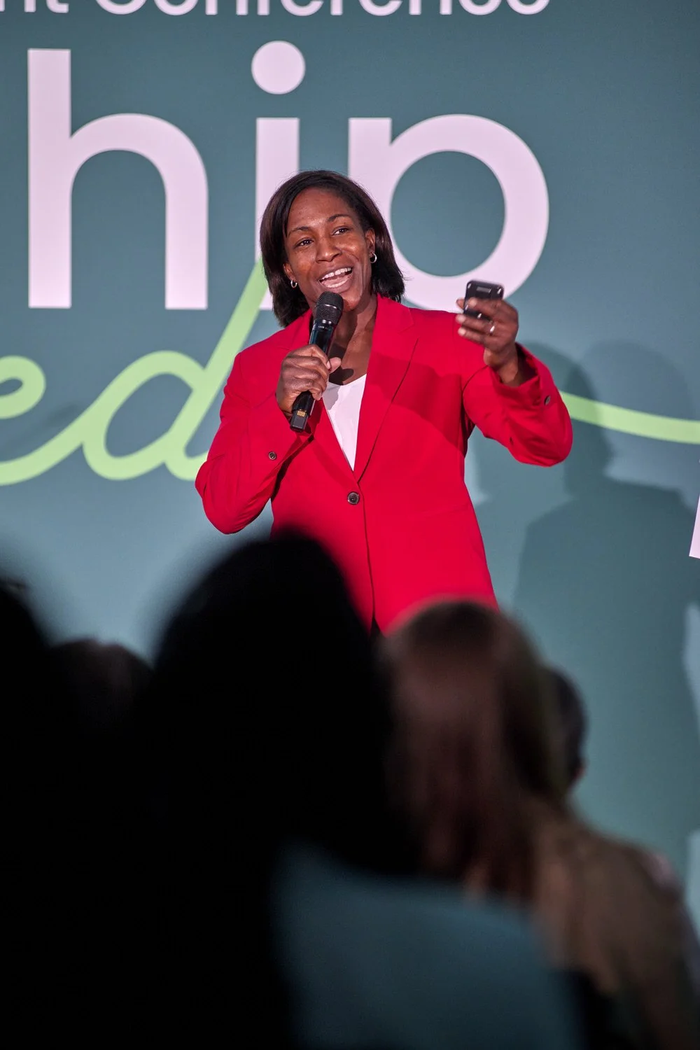 Lady in red jacket speaking on stage at a professional event.