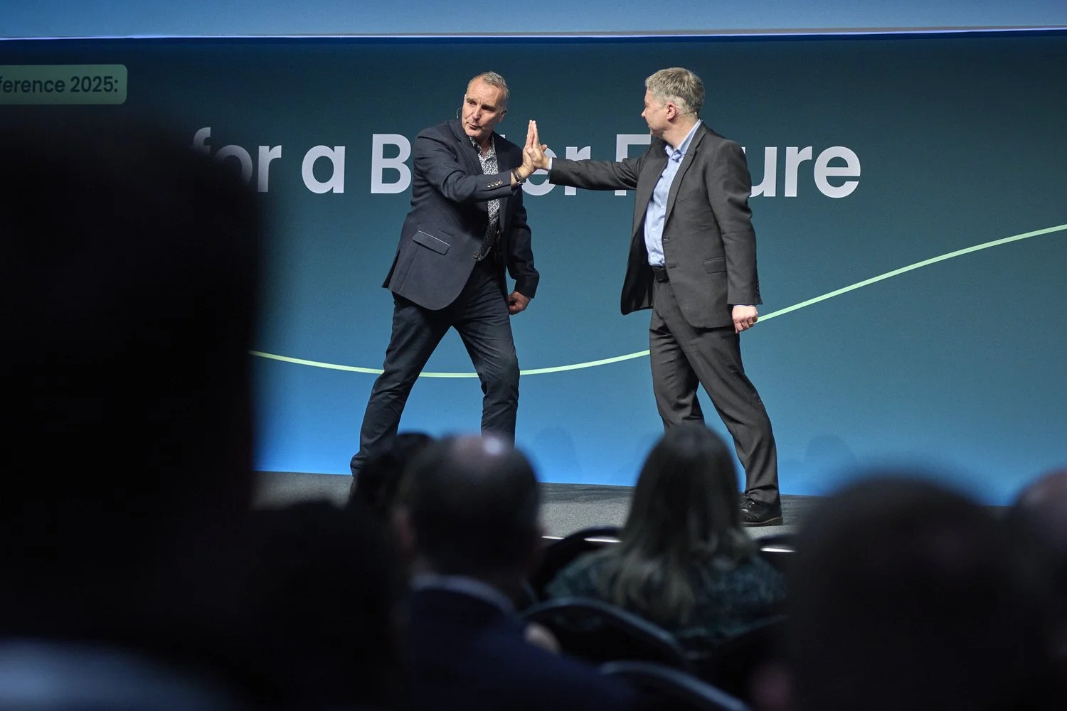 Two men on stage demonstrating teamwork bonding gesture.