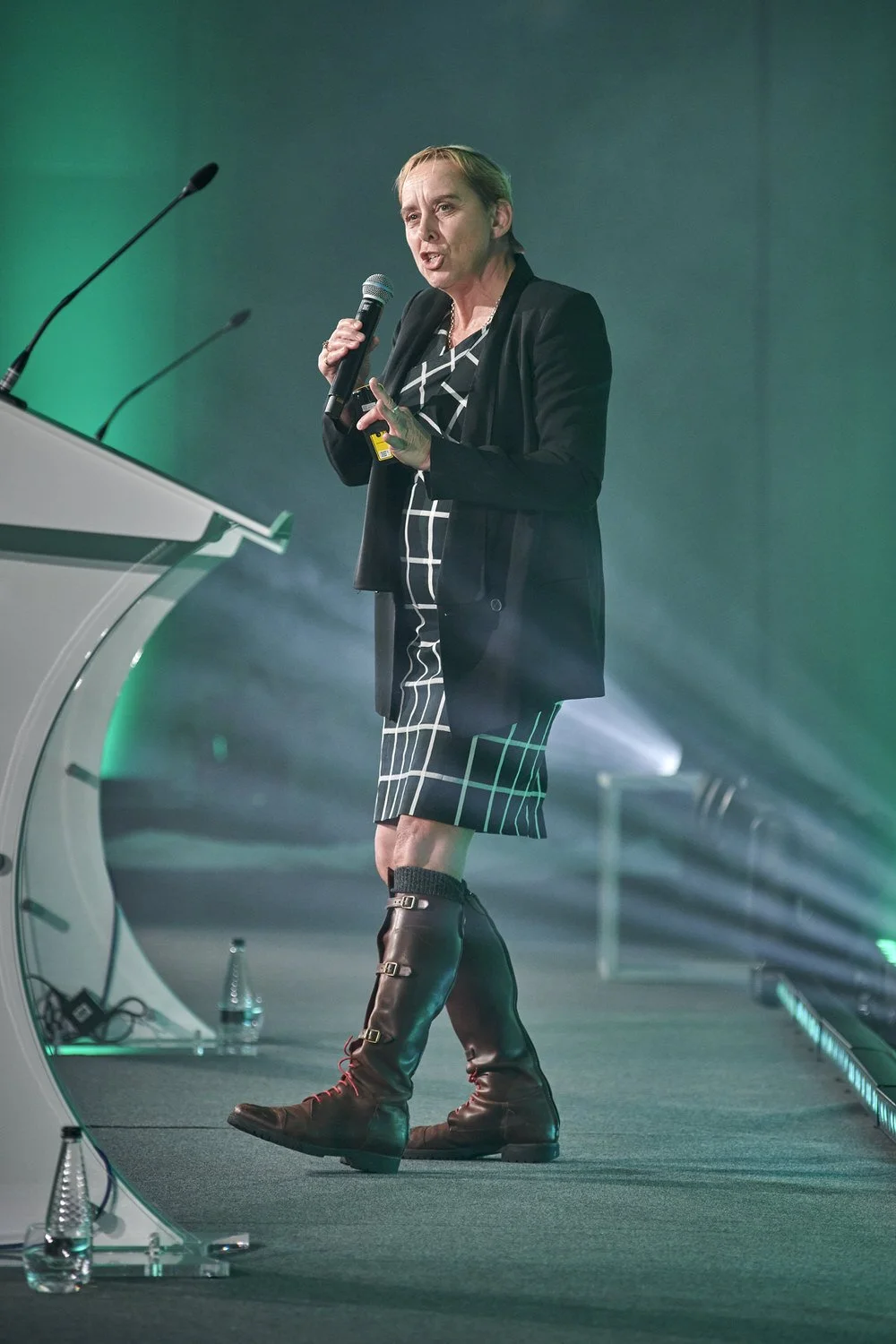 Lady speaking on stage with light beams in the background.