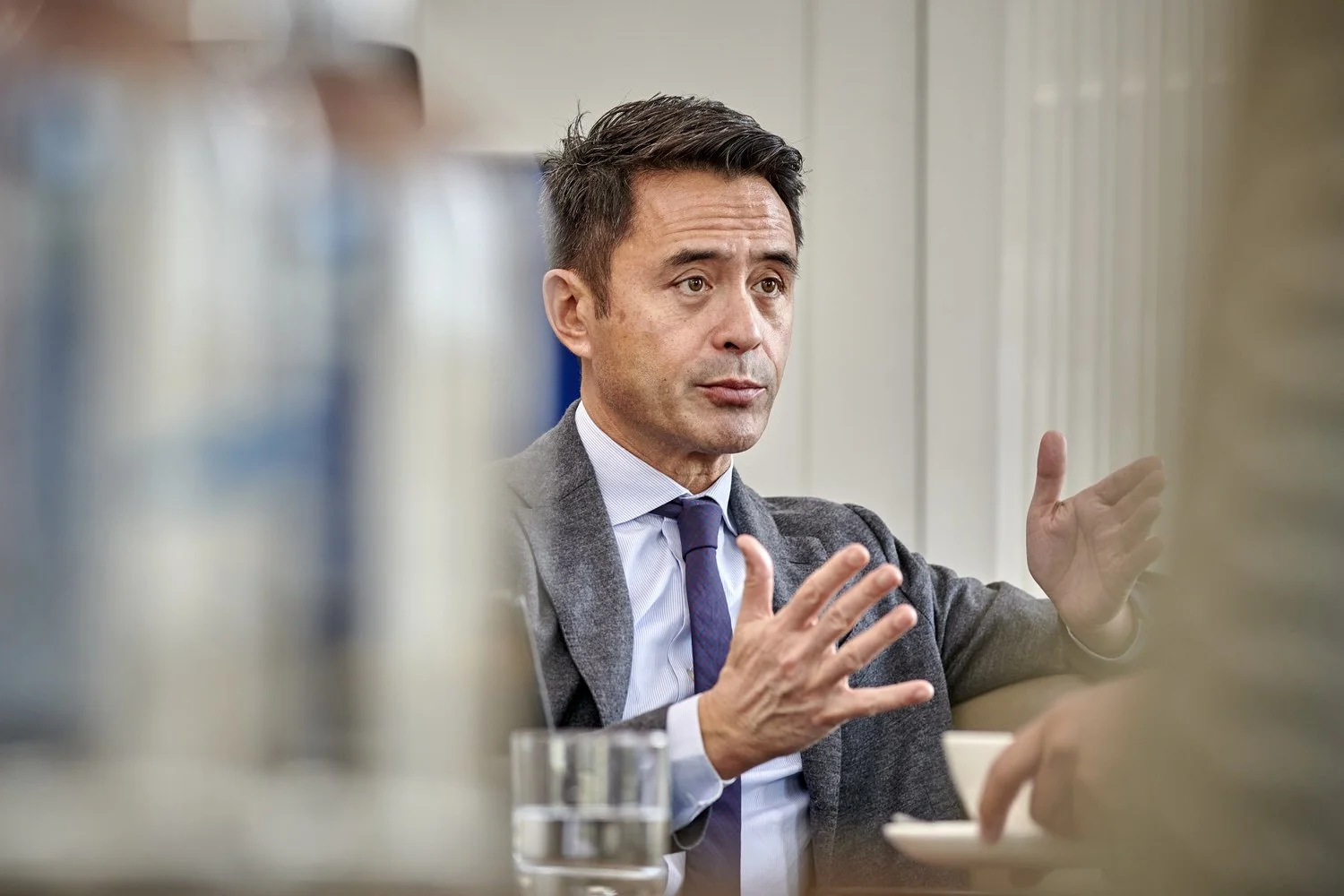 Man gesturing while seen through blurred foreground items during conference.