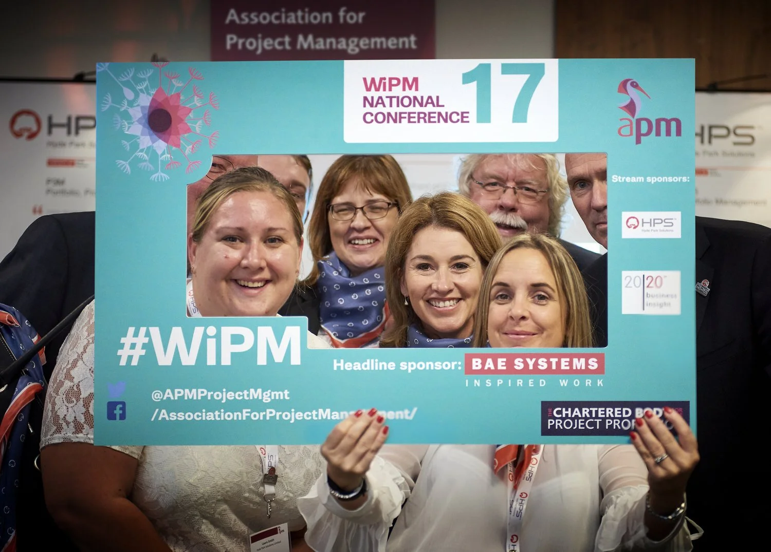 Attendees smiling while looking through a photo frame at the WiPM conference.