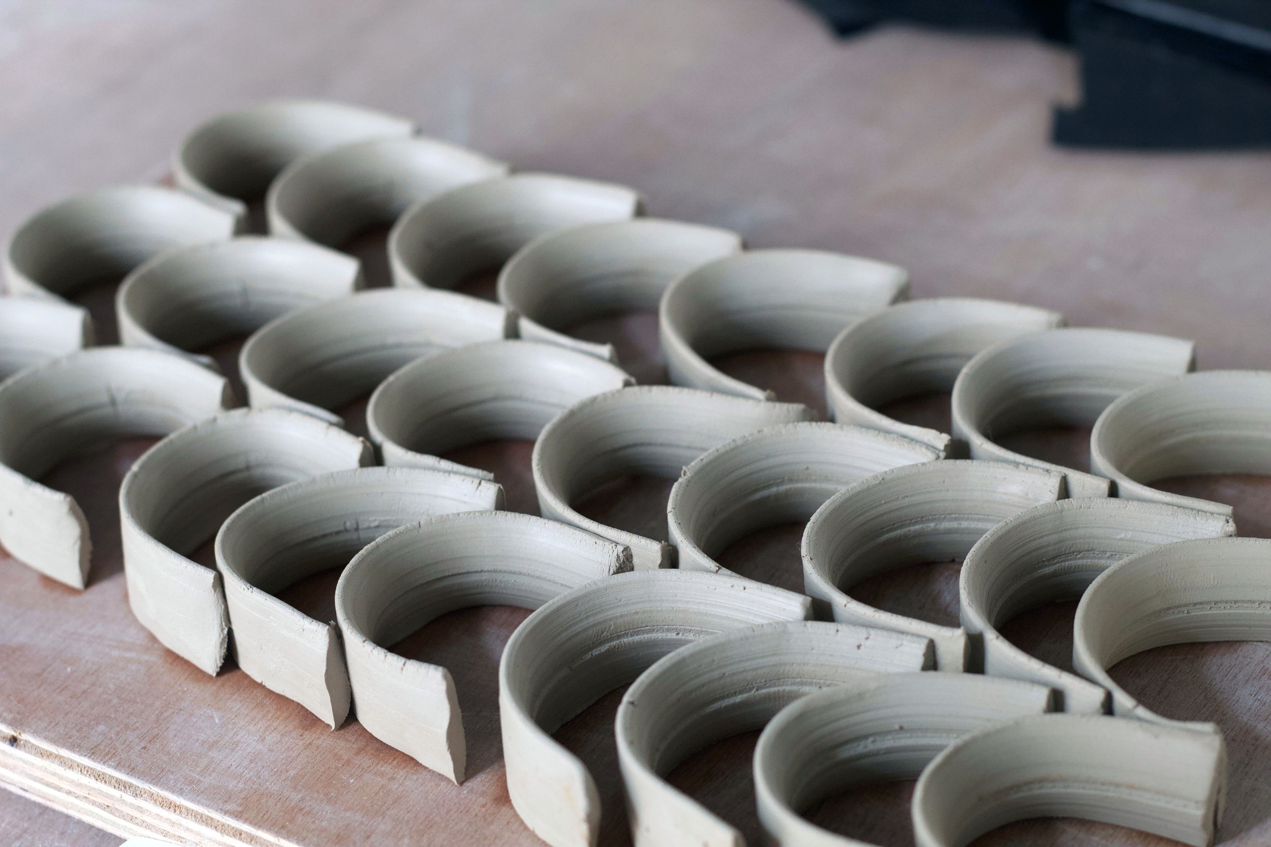 Multiple white ceramic or porcelain ring-shaped parts arranged on a wooden surface, possibly in a manufacturing or crafting setting.
