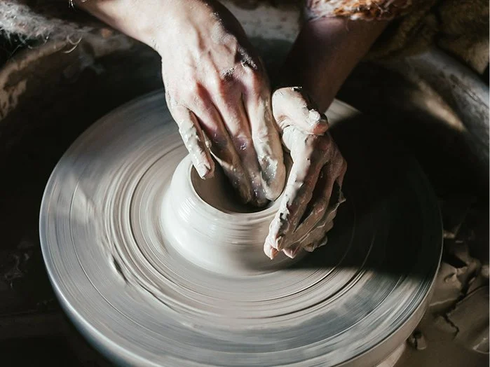 Hands shaping wet clay on a pottery wheel.