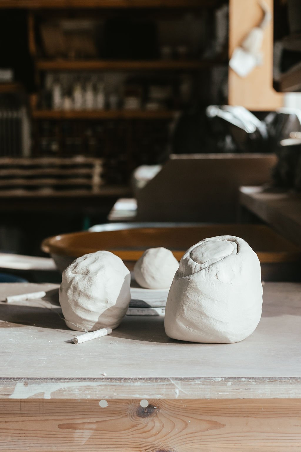 Clay sculptures on a worktable in a pottery studio with shelves in the background.