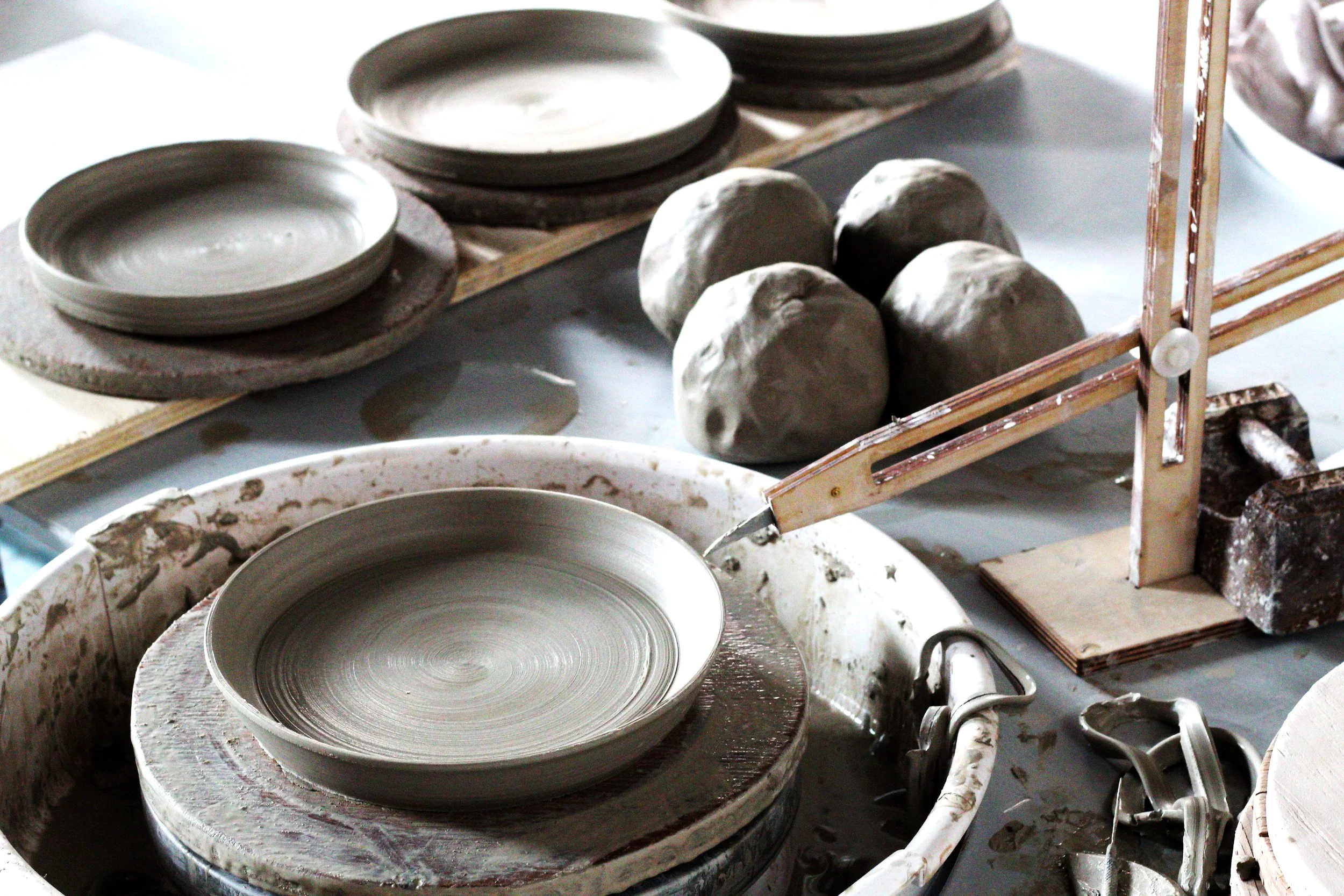 A pottery studio with a spinning wheel, clay bowls, and several lumps of clay on a worktable.