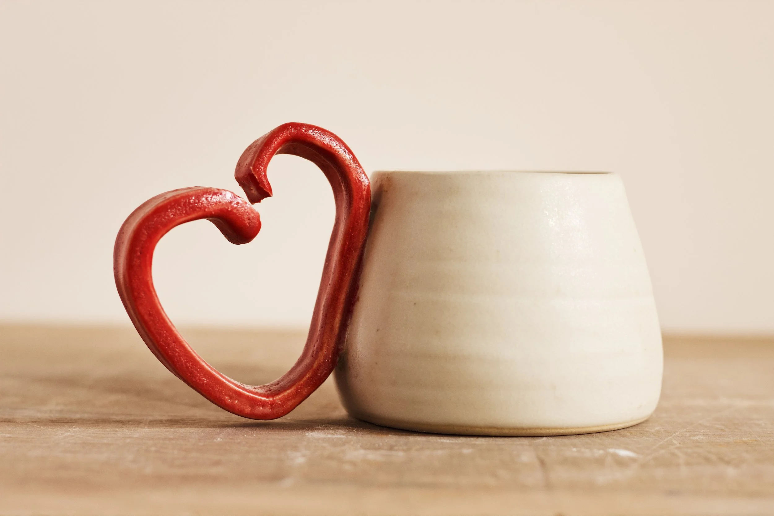 A white ceramic mug with a red heart-shaped handle on a wooden surface.