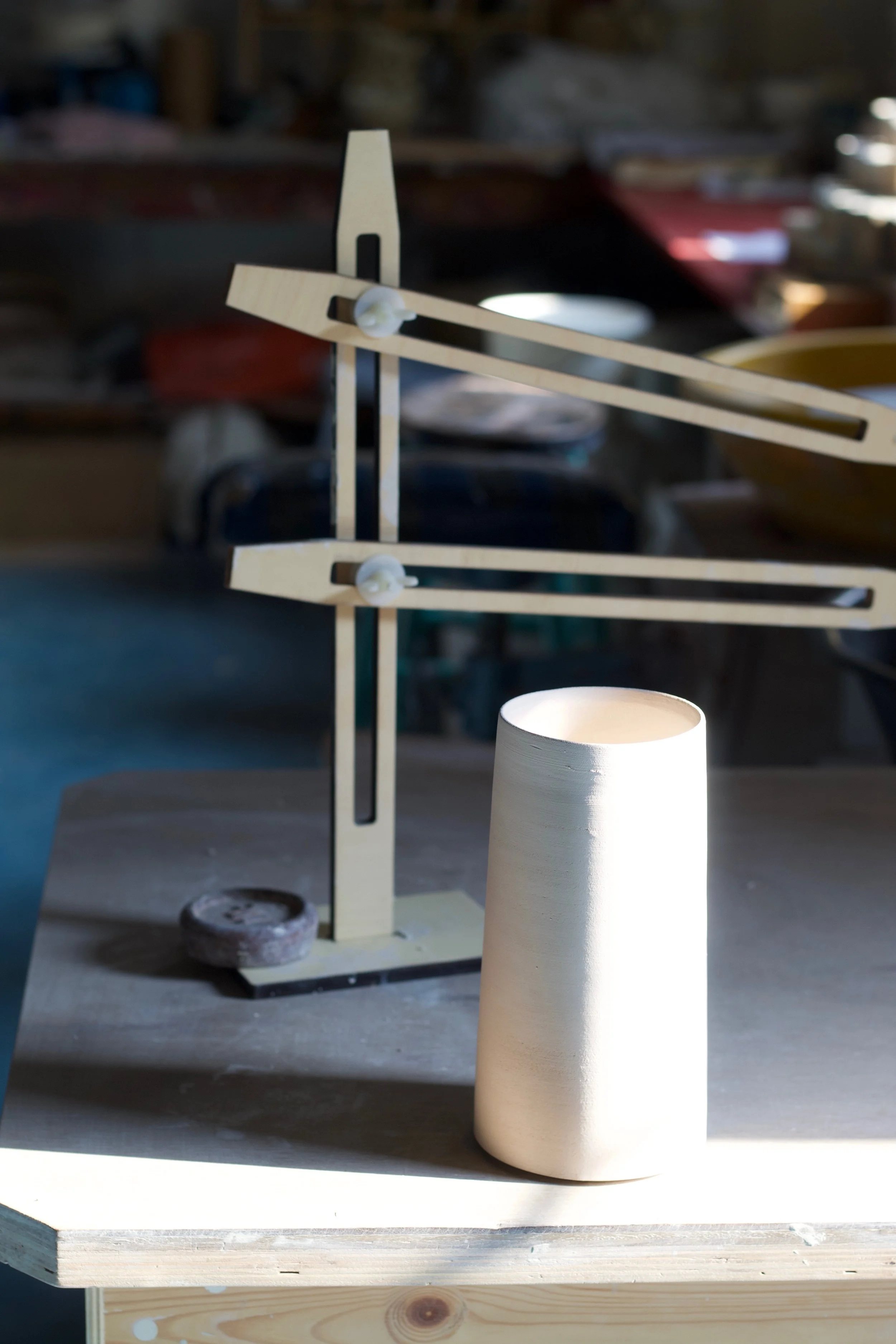 A wooden balance scale with a ceramic cup or vase on a table in a workshop or studio setting.