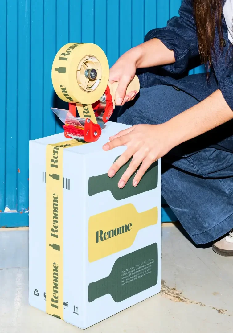 Person sealing a cardboard box with yellow tape that has the word 'Remove' and an arrow, while wearing dark clothing.