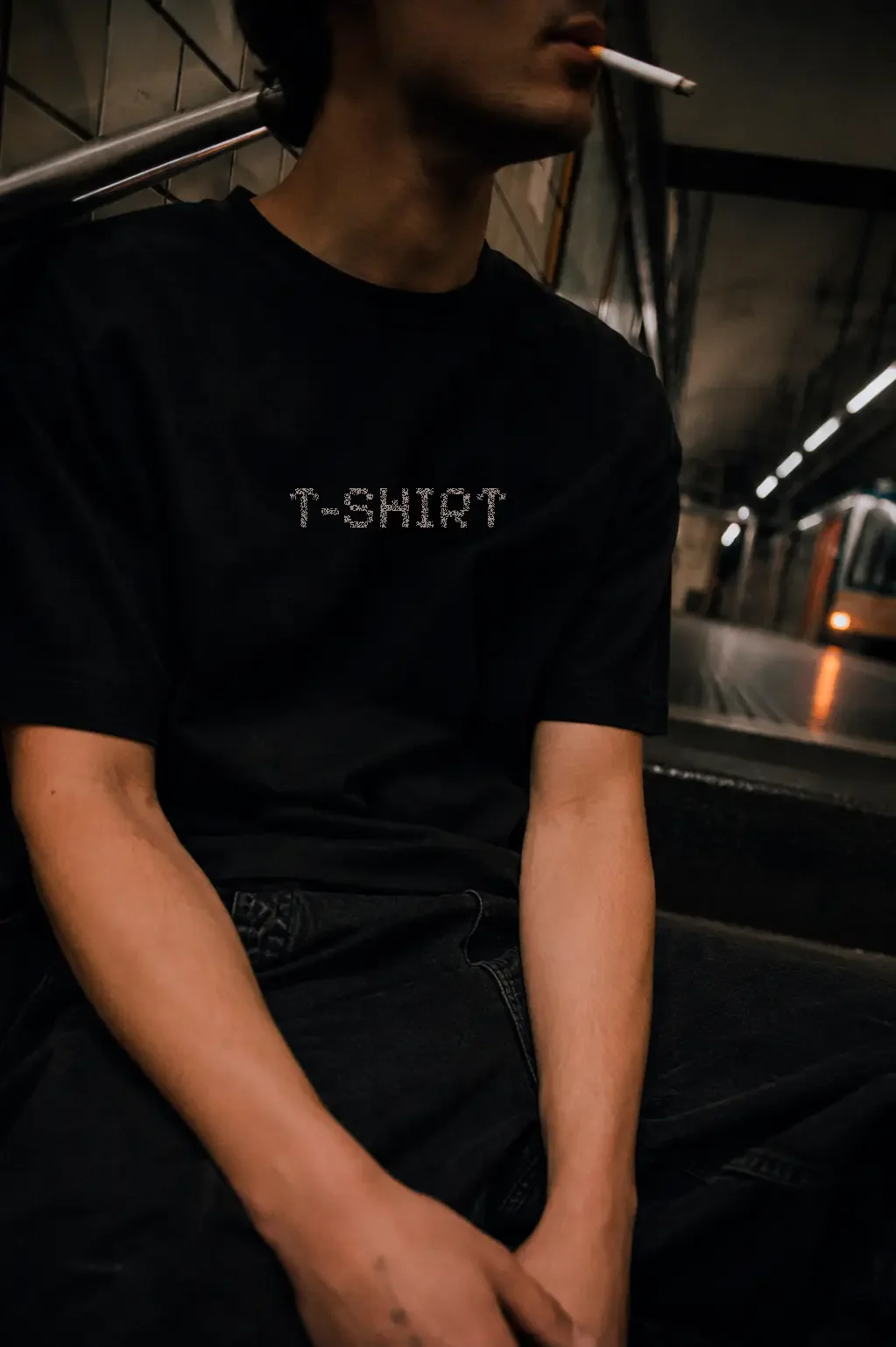 Person sitting on a subway train wearing a black t-shirt with 'T-SHIRT' written on it, smoking a cigarette, with a subway train visible in the background.
