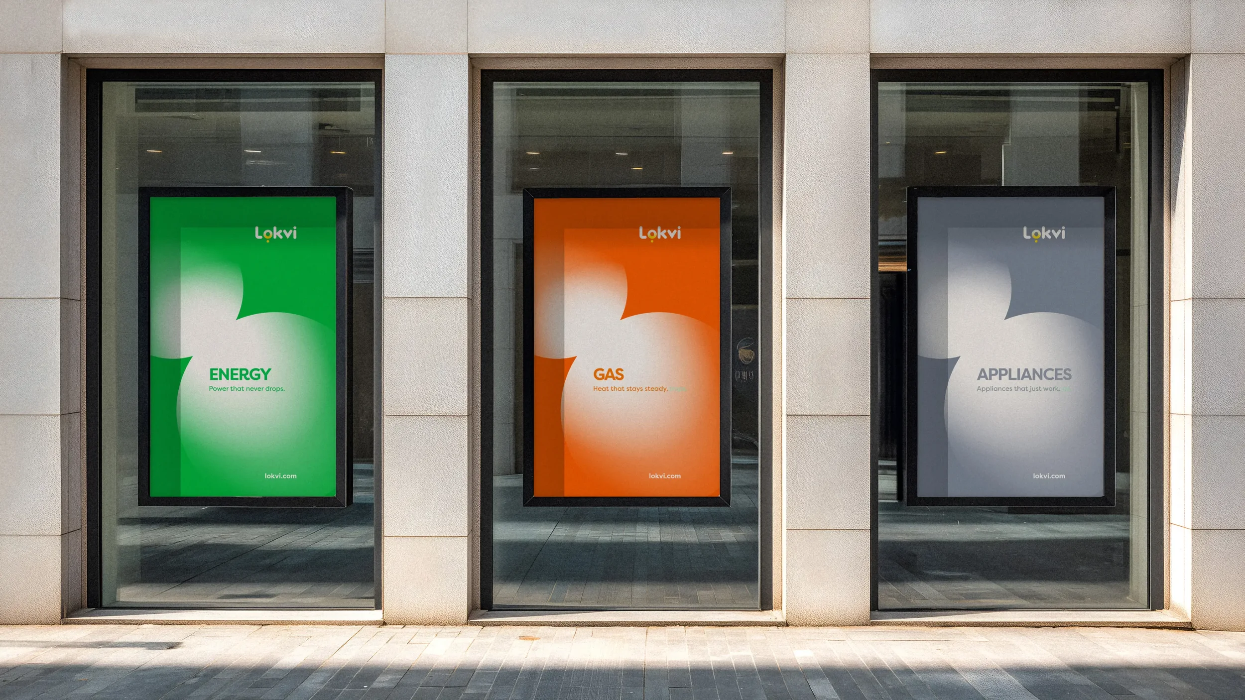 Three digital posters on a building window display. The first has a green background with the word 'ENERGY' and the tagline 'Power that never drops.' The middle has an orange background with the word 'GAS' and the tagline 'Heat that stays steady.' The third has a gray background with the word 'APPLIANCES' and the tagline 'Appliances that just work.'