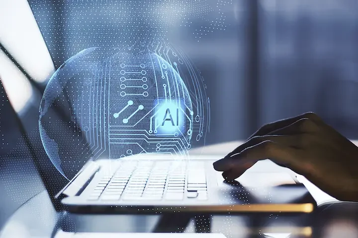 Close-up of a person's hand typing on a laptop with a digital hologram of a globe and AI symbols floating above the keyboard.