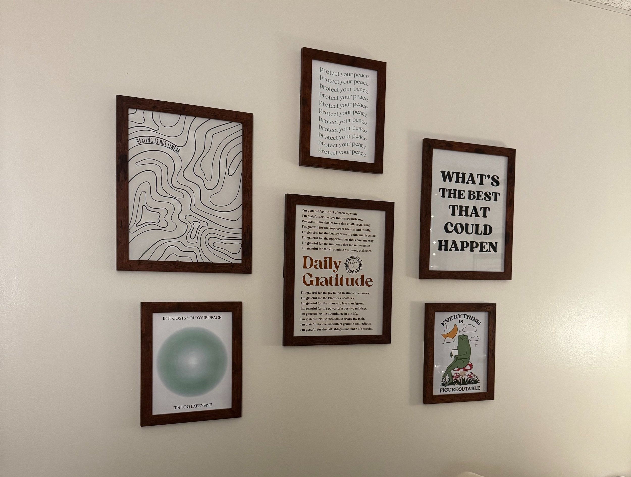 Gallery wall with six framed prints featuring motivational quotes, abstract designs, and illustrations, accenting a beige wall.
