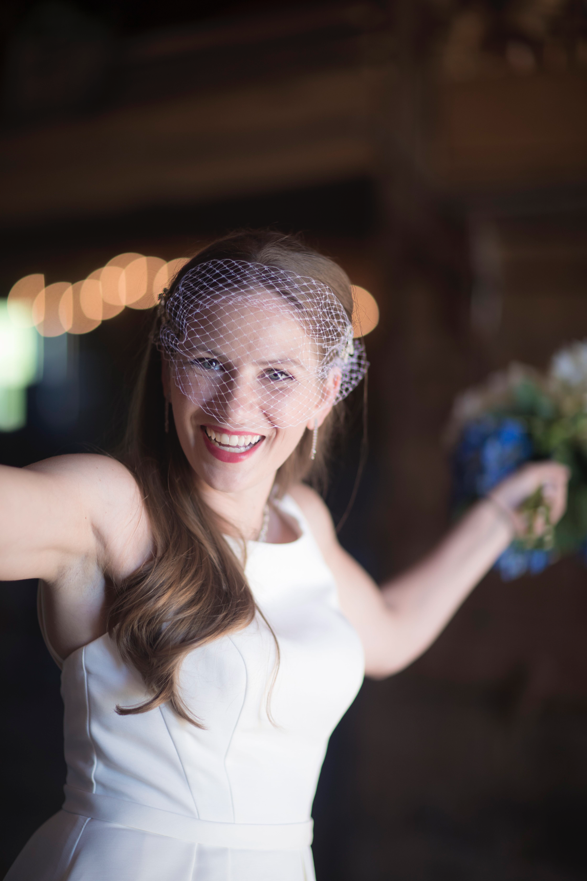 Smiling bride wearing a white dress and birdcage veil, holding a bouquet.