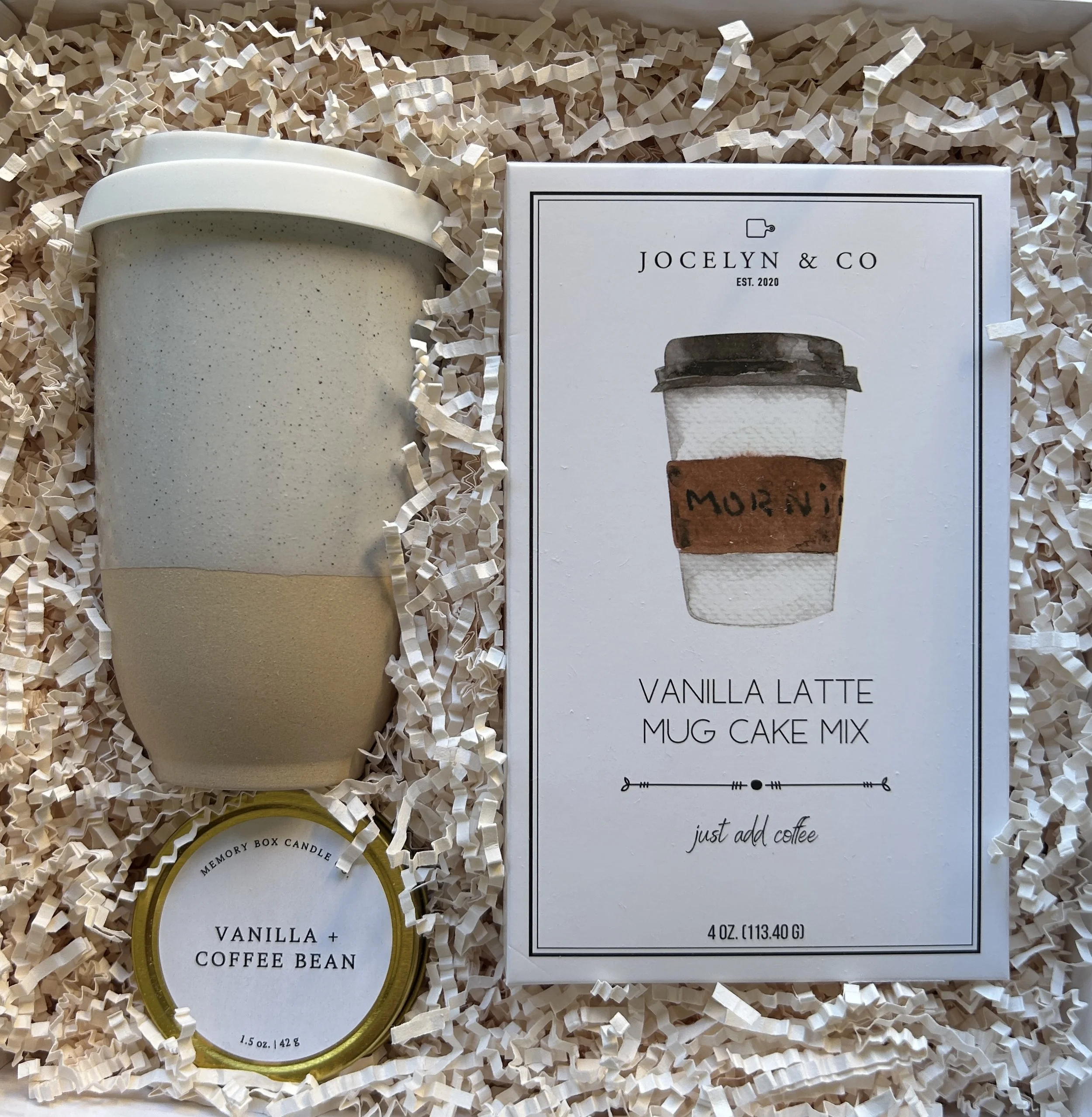 A gift box containing a a ceramic travel mug vanilla latte mug cake vanilla & coffee bean travel candle all placed in a gift box with ivory crinkle paper