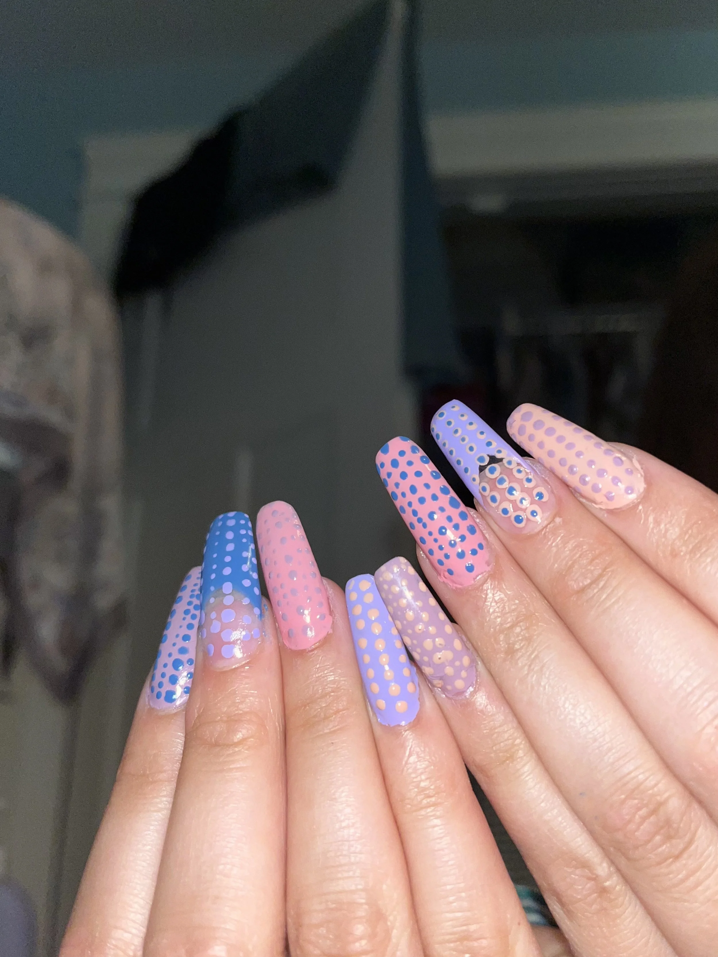 Nails with pink and purple base colors decorated with blue and golden polka dots.