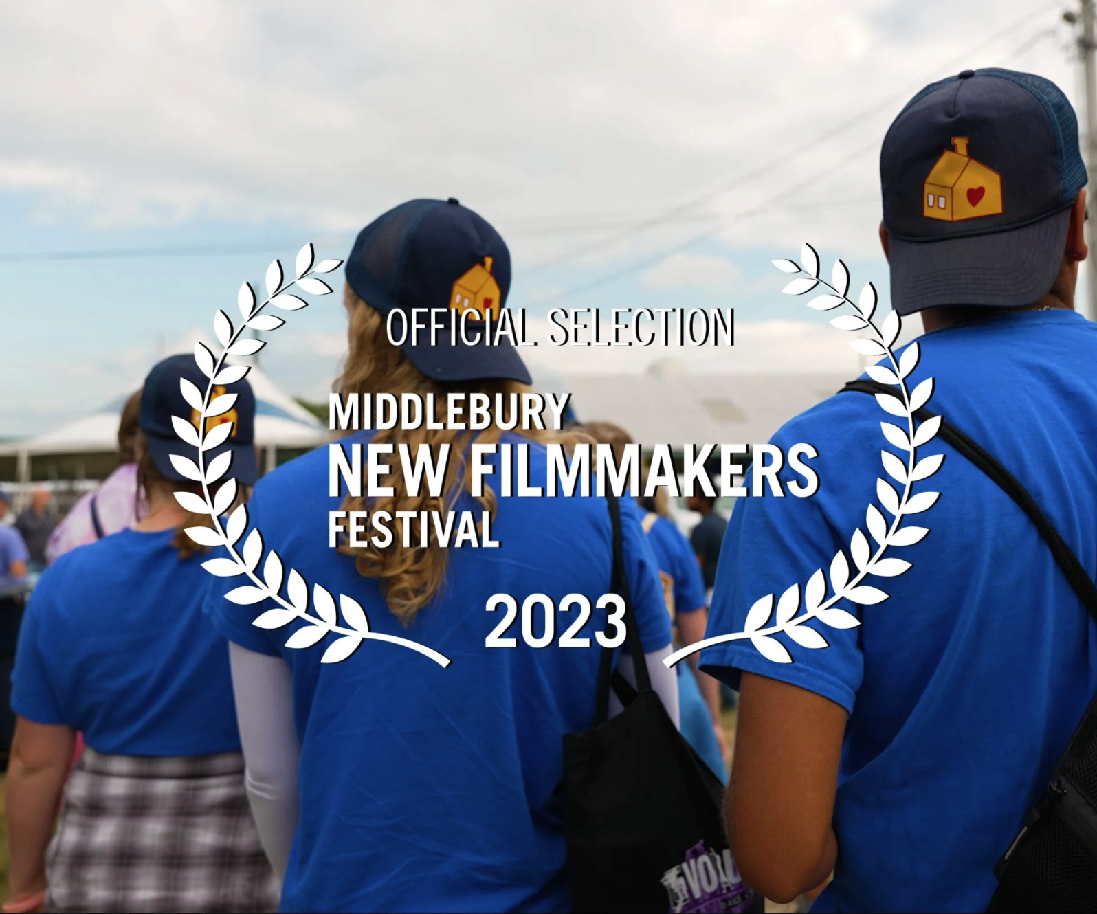 People wearing blue shirts and caps with a house logo, attending the Middlebury New Filmmakers Festival 2023 outdoors.