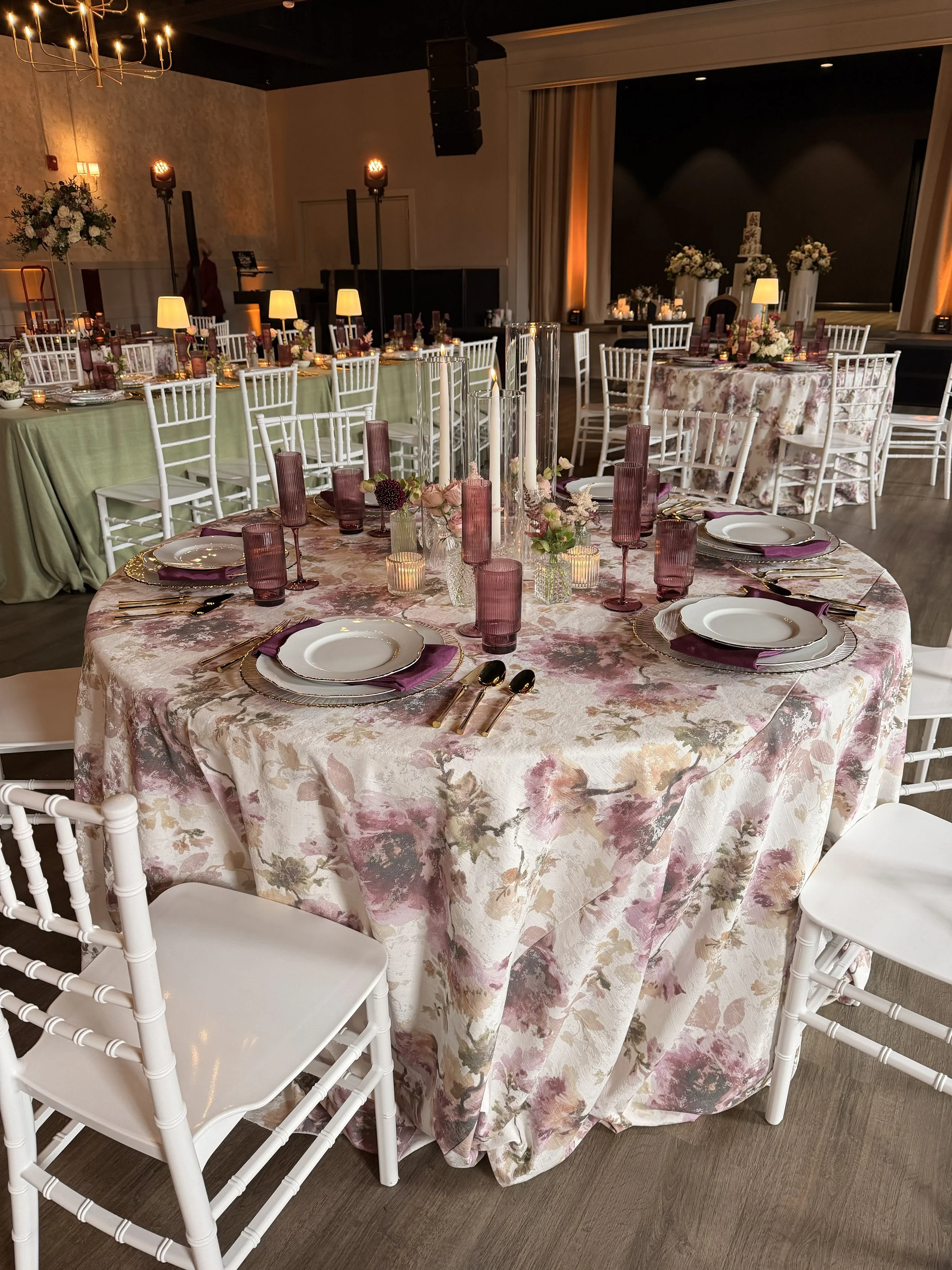 Wedding venue with a wooden ceiling and walls, decorated with flowing white fabric and string lights. A white wedding dress hangs from the ceiling in the center, with chandeliers and a bright doorway at the back.