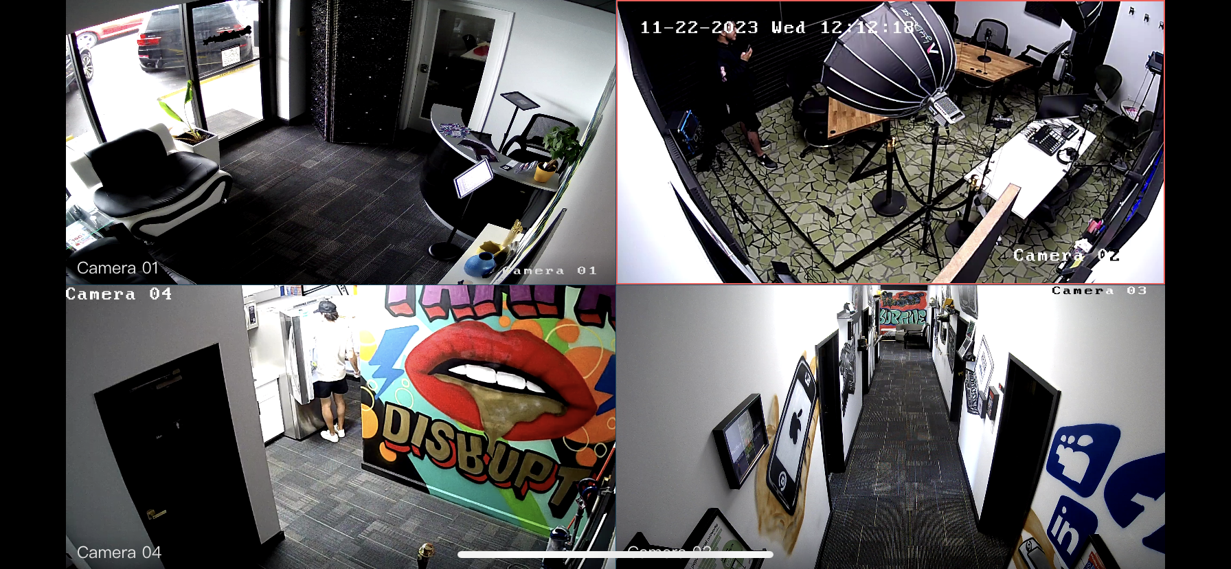 Four surveillance camera feeds showing the interior of a modern office space. The first feed displays a waiting area with black leather chairs and a front door. The second shows a meeting room with a wooden table, black chairs, and photography equipment. The third captures a hallway with vibrant graffiti art and a person entering an elevator. The fourth reveals a corridor with framed artwork and social media icons on the wall.