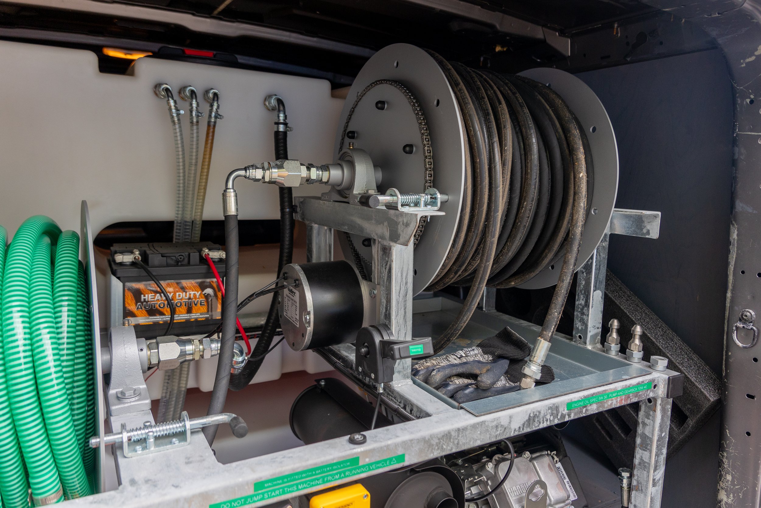 Close-up of industrial hoses and equipment inside a vehicle, including a reel of black hoses, various metal fittings, and electronic devices.