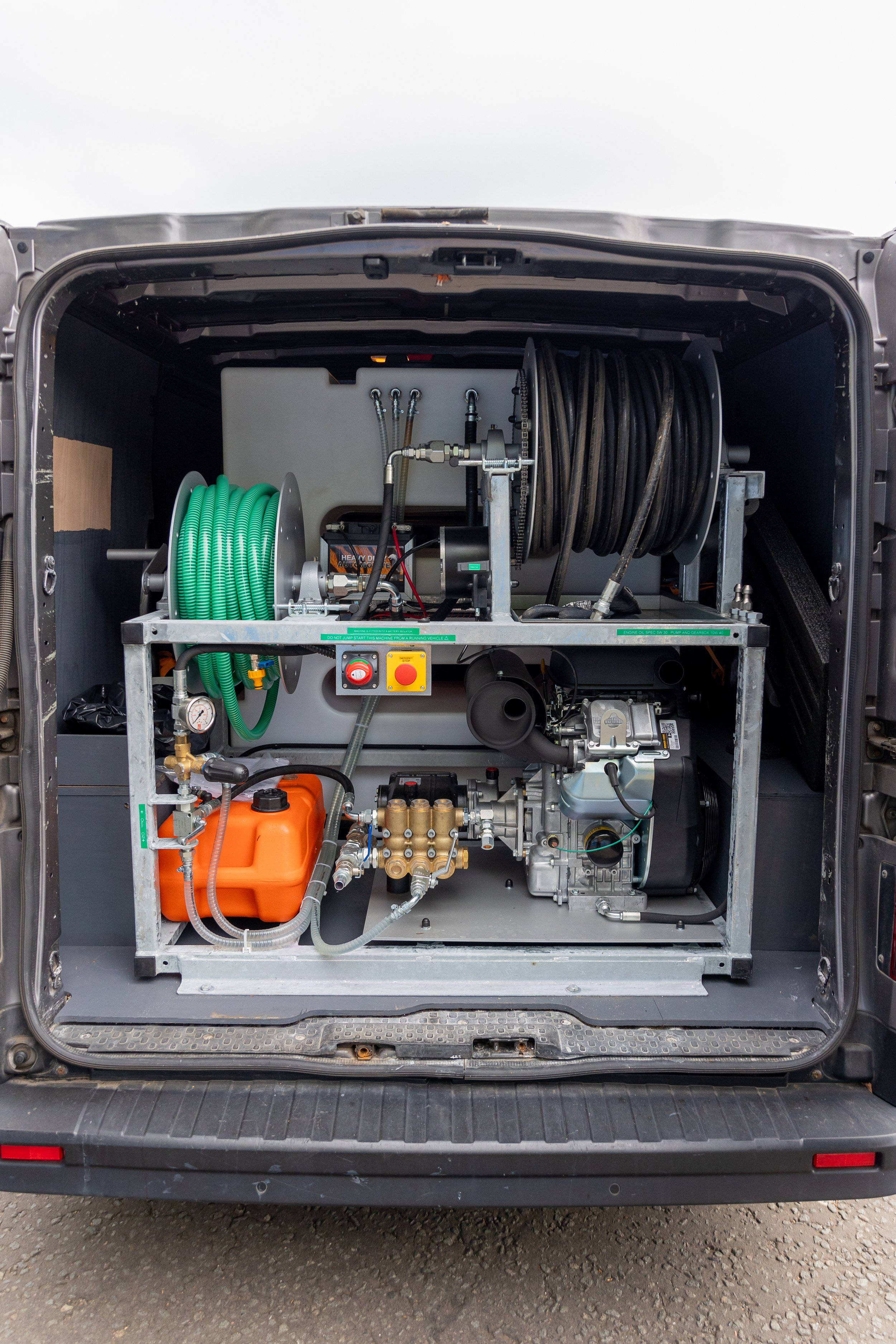 Back of a van showing a mounted water or industrial cleaning machine with hoses, gauges, and mechanical components.