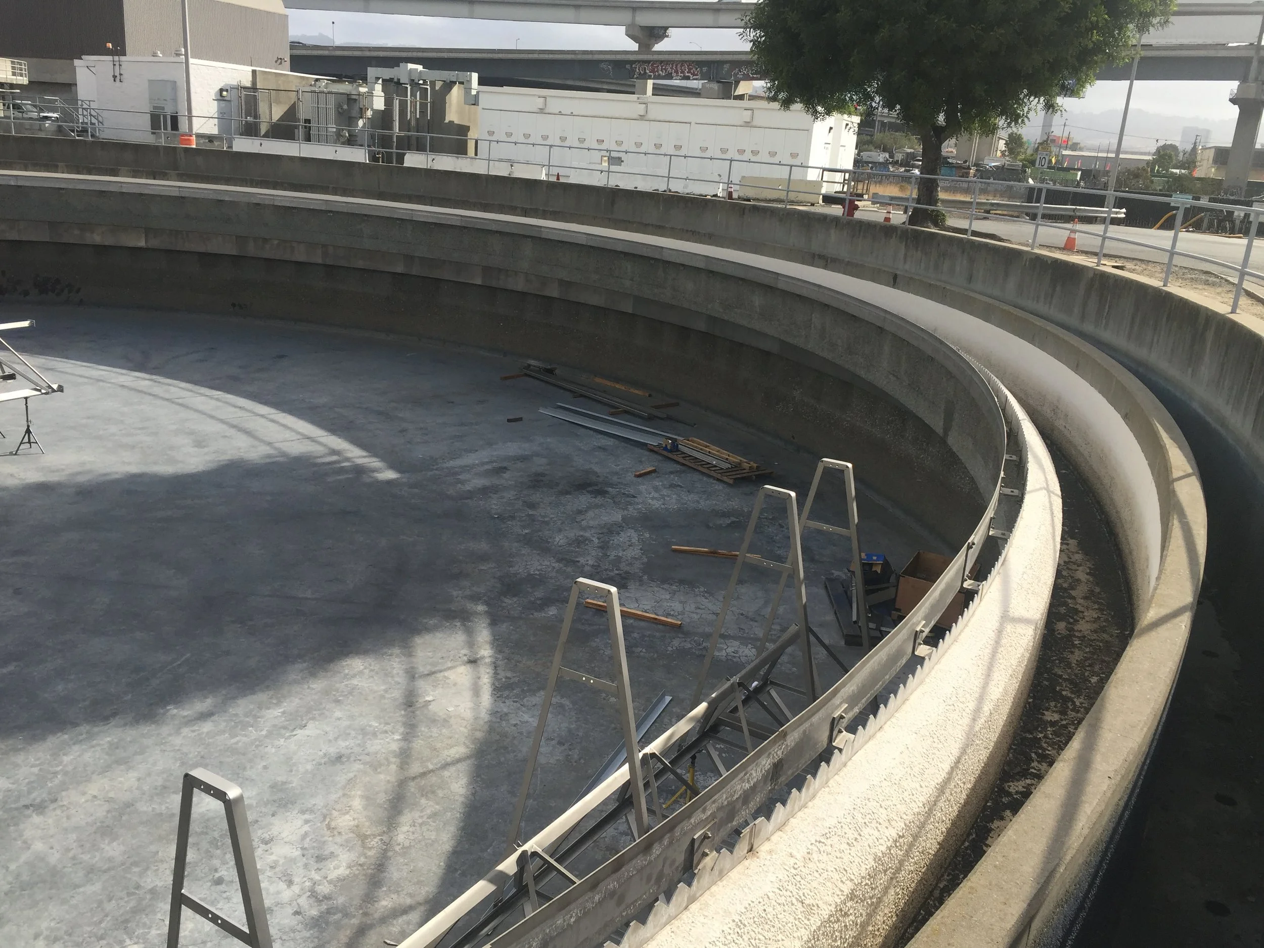 Wide-angle view of the empty clarifier tank at EBMUD showing the tunnel entrance and repair site along the west perimeter, with ladders and construction materials staged inside.