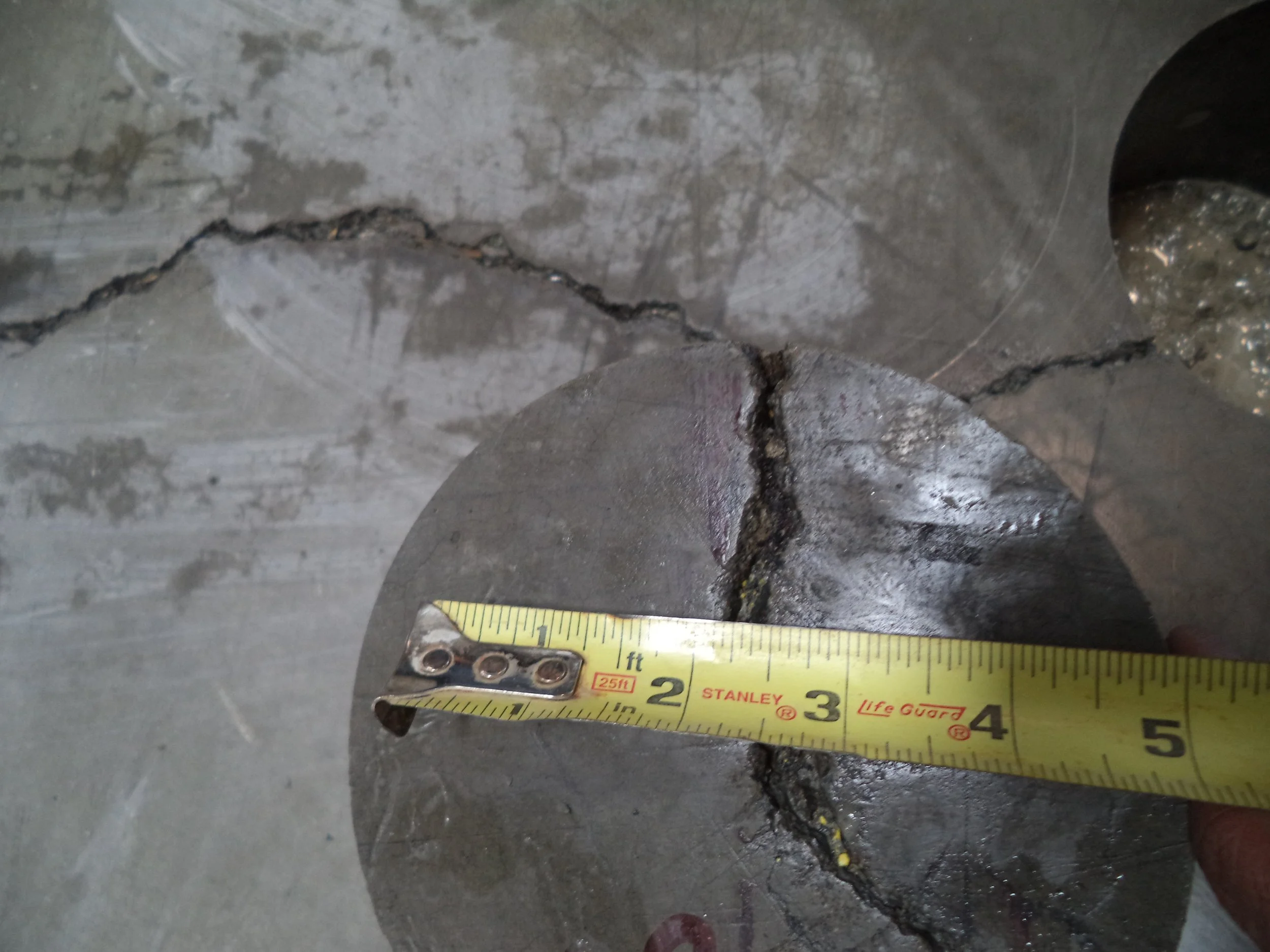 Irregular slab crack photographed at a core with tape measure for scale.