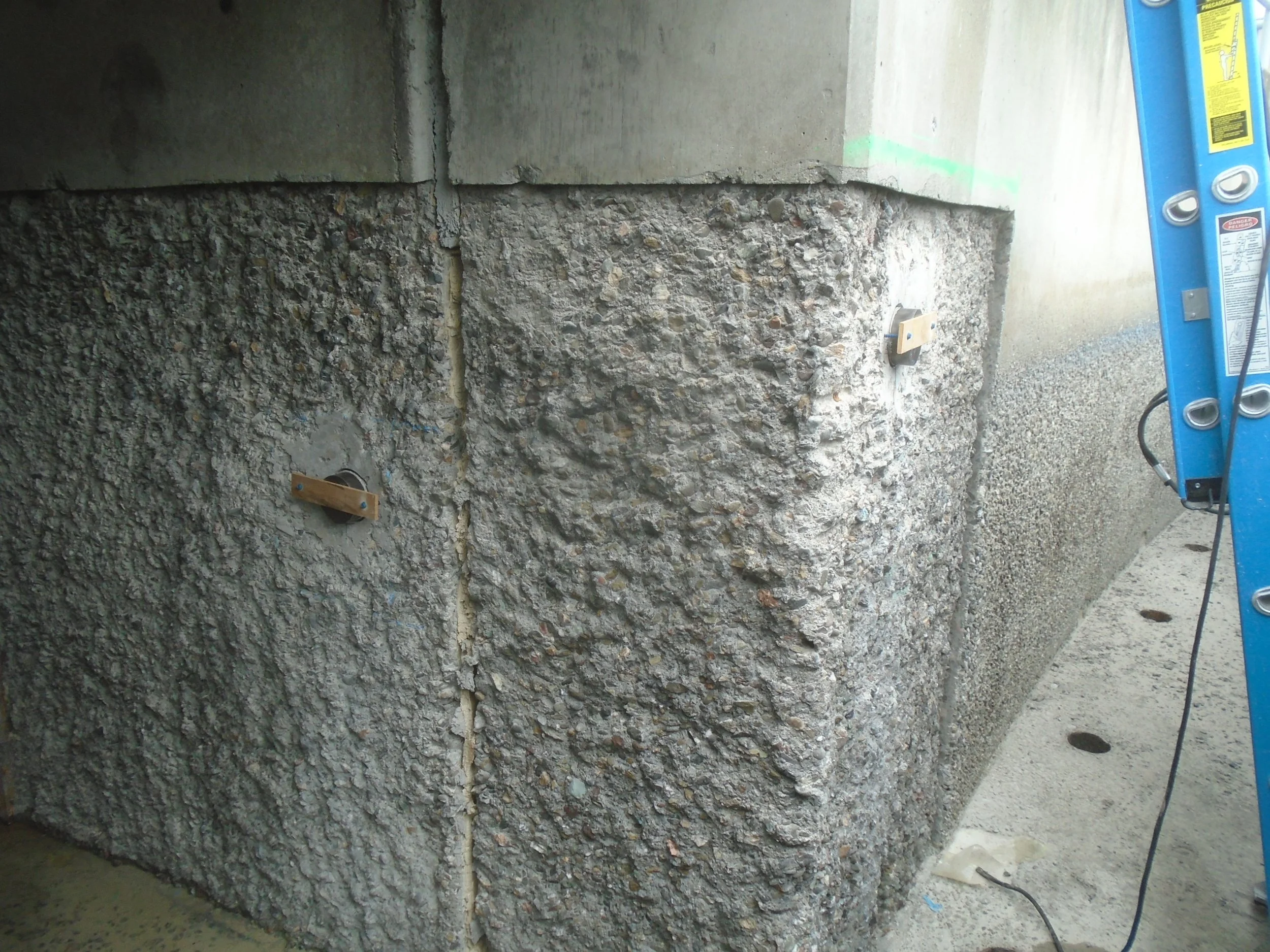 Close-up of a vertical concrete wall at the EBMUD clarifier showing a test location with exposed aggregate, illustrating a roughened surface prepared for tensile pull-off bond testing.