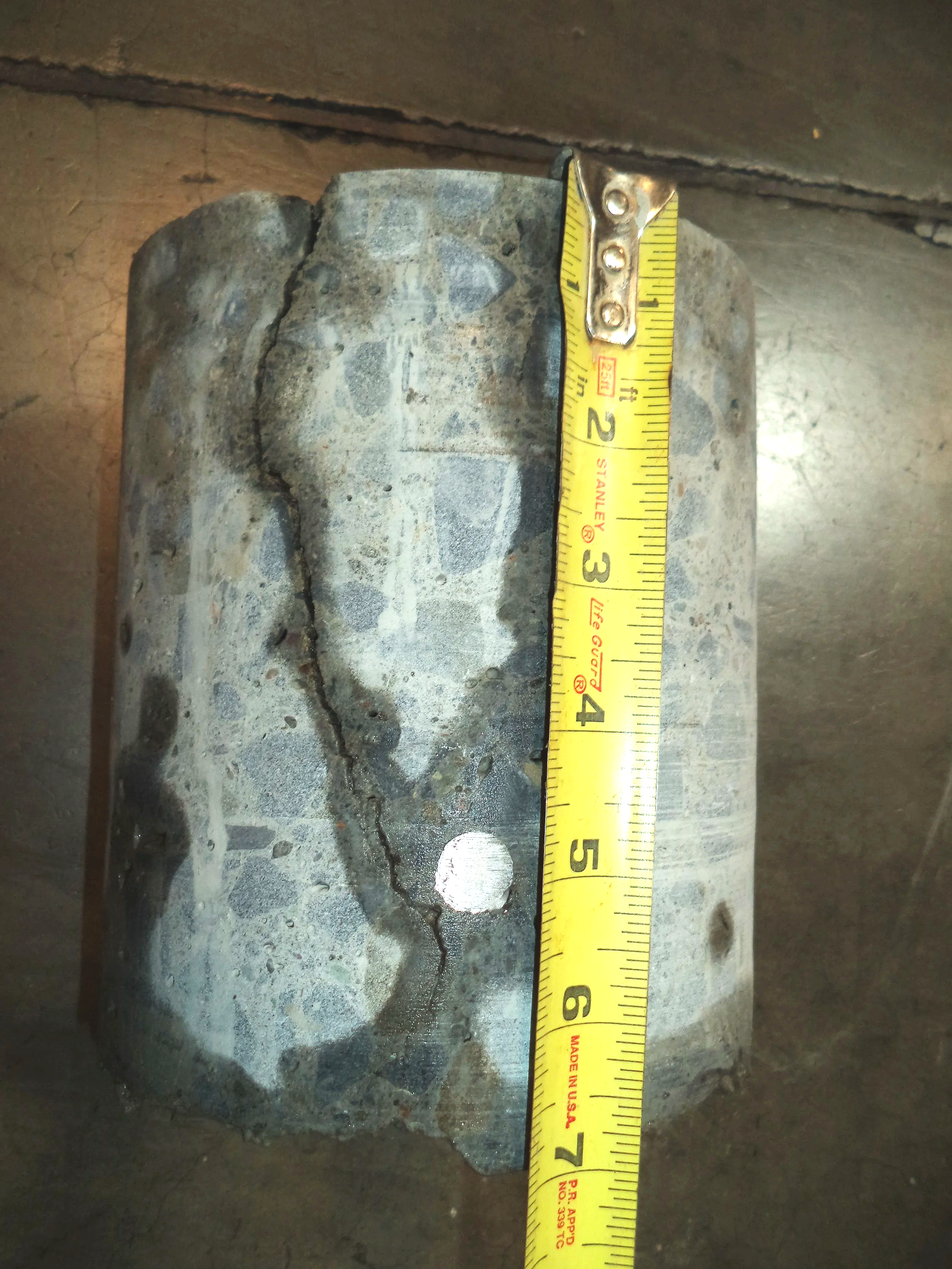 Concrete core from warehouse slab used to verify reinforcing steel located low in the section, with tape measure for scale.