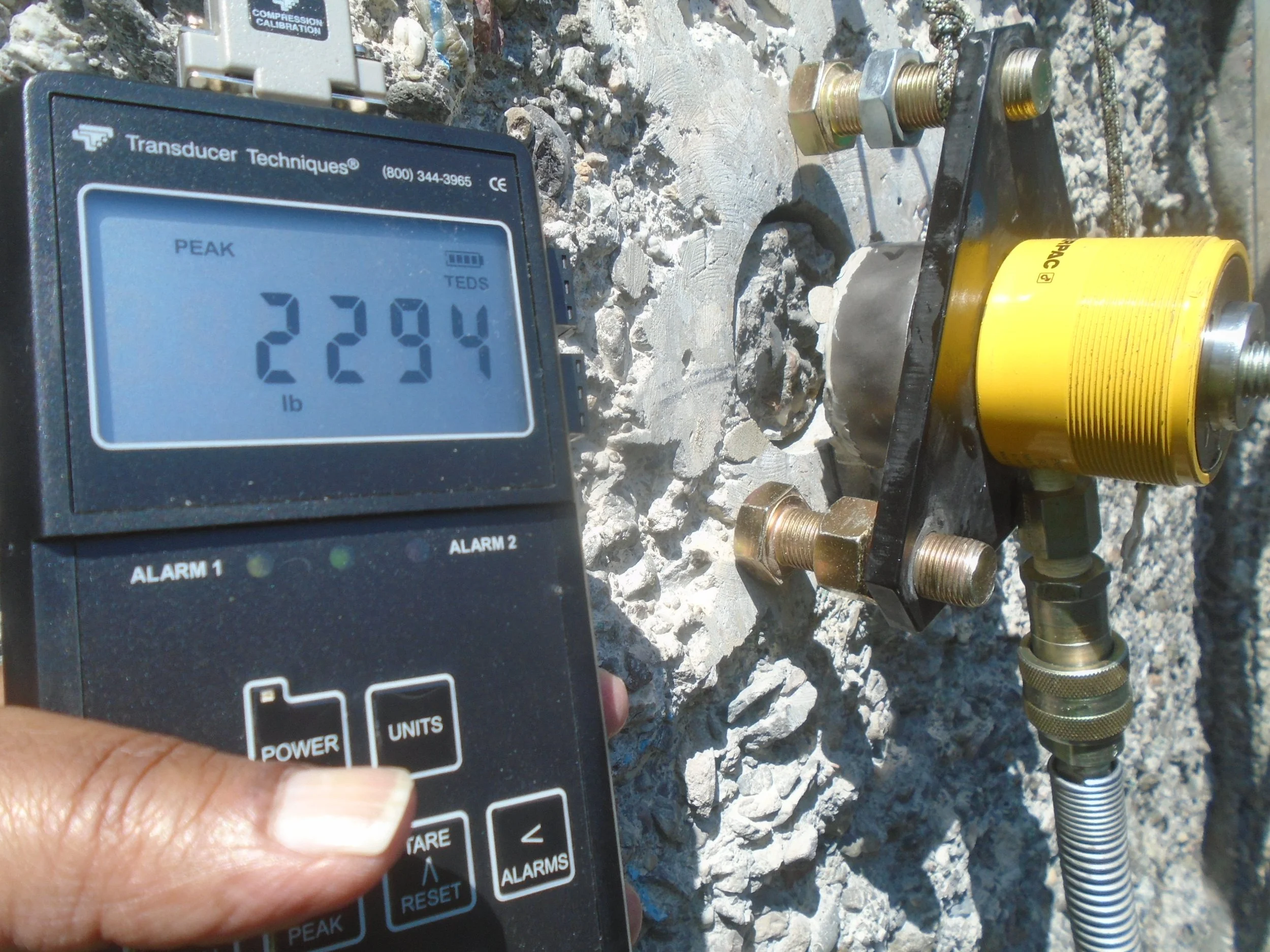 Close-up of a digital load cell displaying a tensile load of 2,294 pounds during a pull-off test on a prepared concrete surface at the EBMUD clarifier, demonstrating bond strength of the repair mortar.