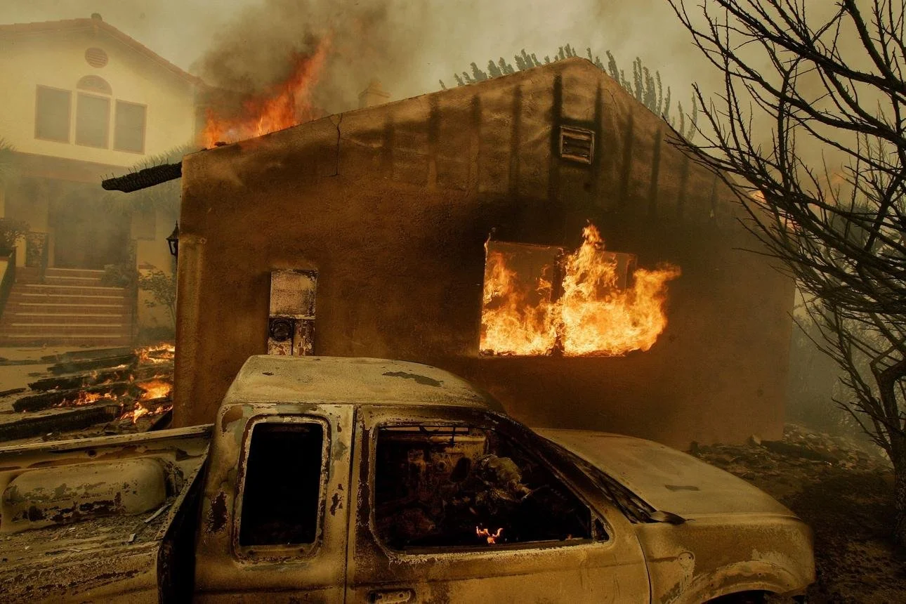 Residential home burning during a California wildfire, demonstrating how wind-driven embers can ignite structures and surrounding combustible materials.