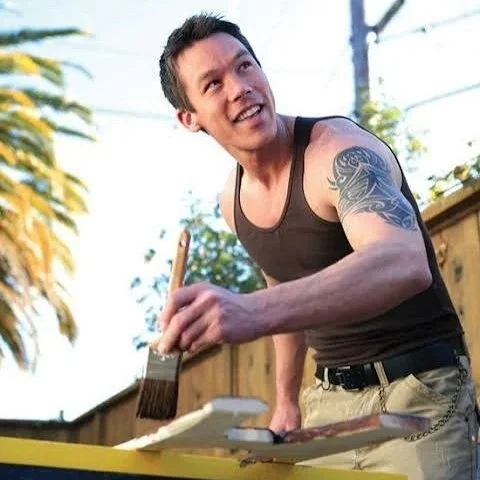 Man painting outdoors with a paintbrush, smiling.