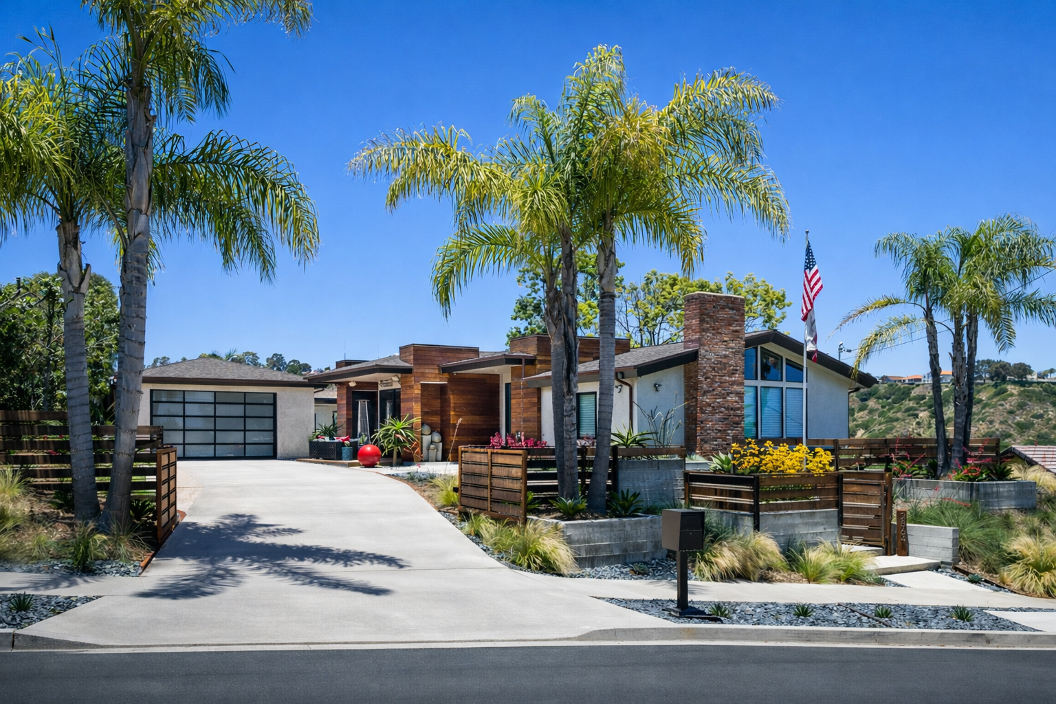 Modern house with palm trees, a curved driveway, and a front yard with various plants and flowers under a clear blue sky.  Custom landscaper contractor near me in La Jolla