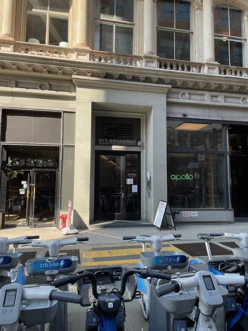 Street view of a building with storefronts, including a Citi Bike station and a business named Apollo, with bicycles in the foreground.