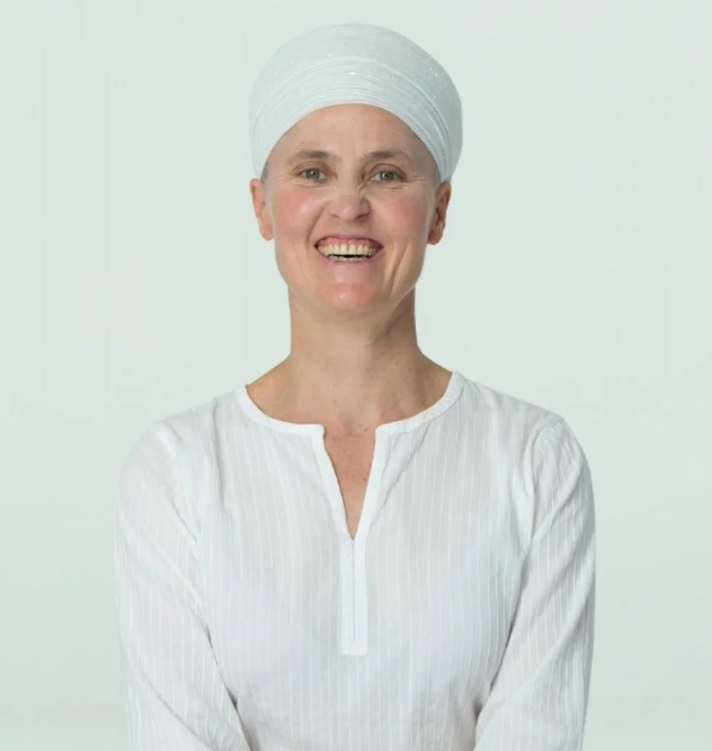 Simran Kaur wearing a white turban and a white blouse, smiling against a plain light background.