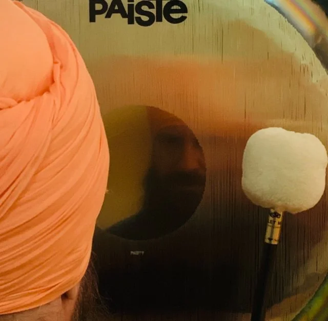 A person wearing an orange turban is playing a gong.