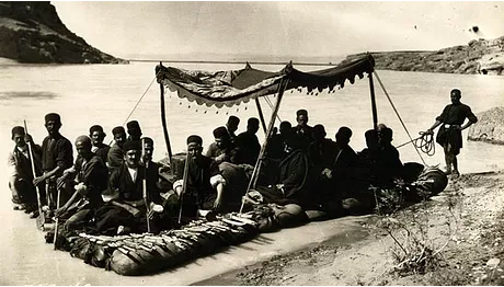 Still from the 1925 film "Grass" shows people on a traditional raft with canopy on a wide river, desert background.
