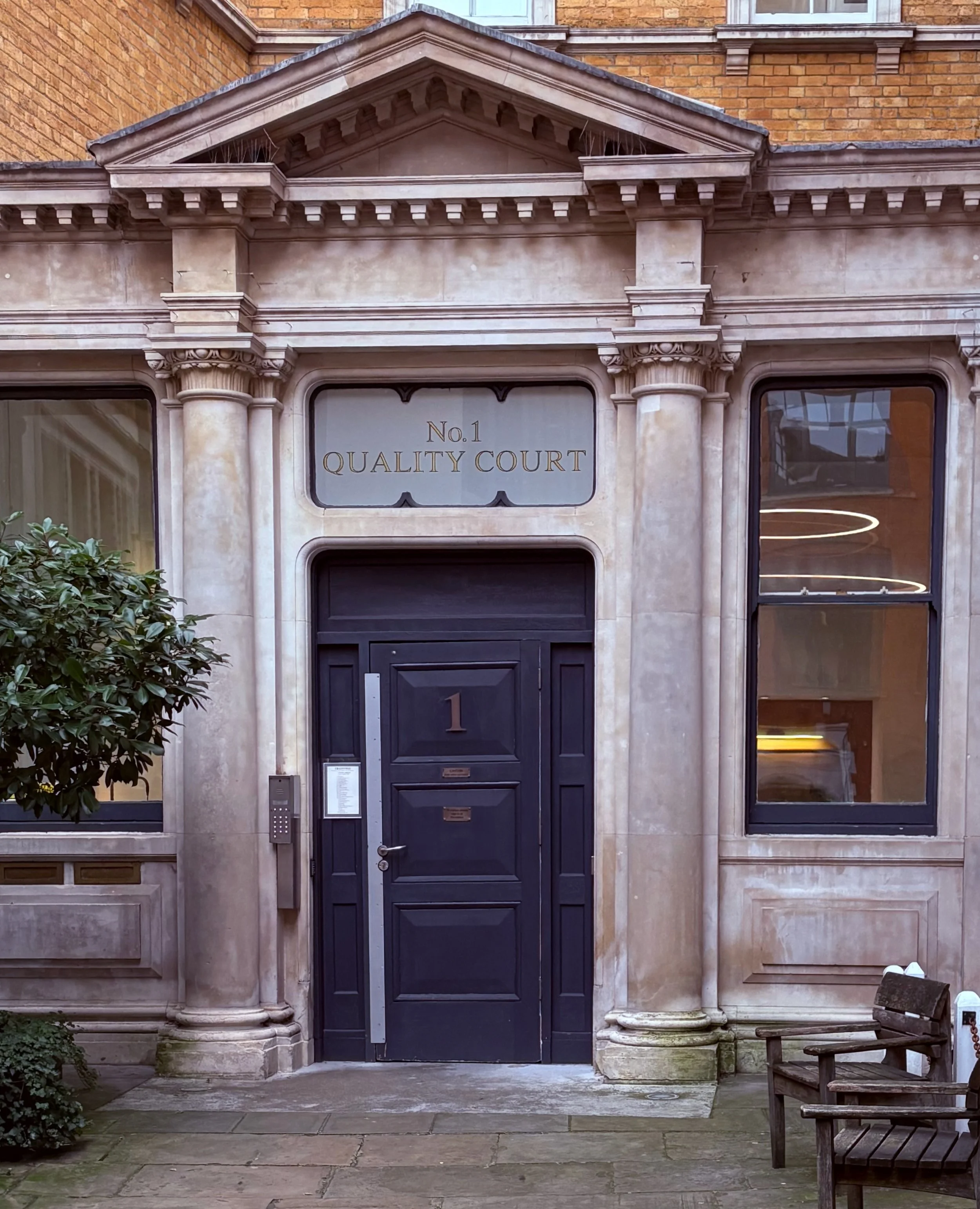Facade of a building with a door numbered 1, sign that reads "No. 1 QUALITY COURT," and classic architectural details.